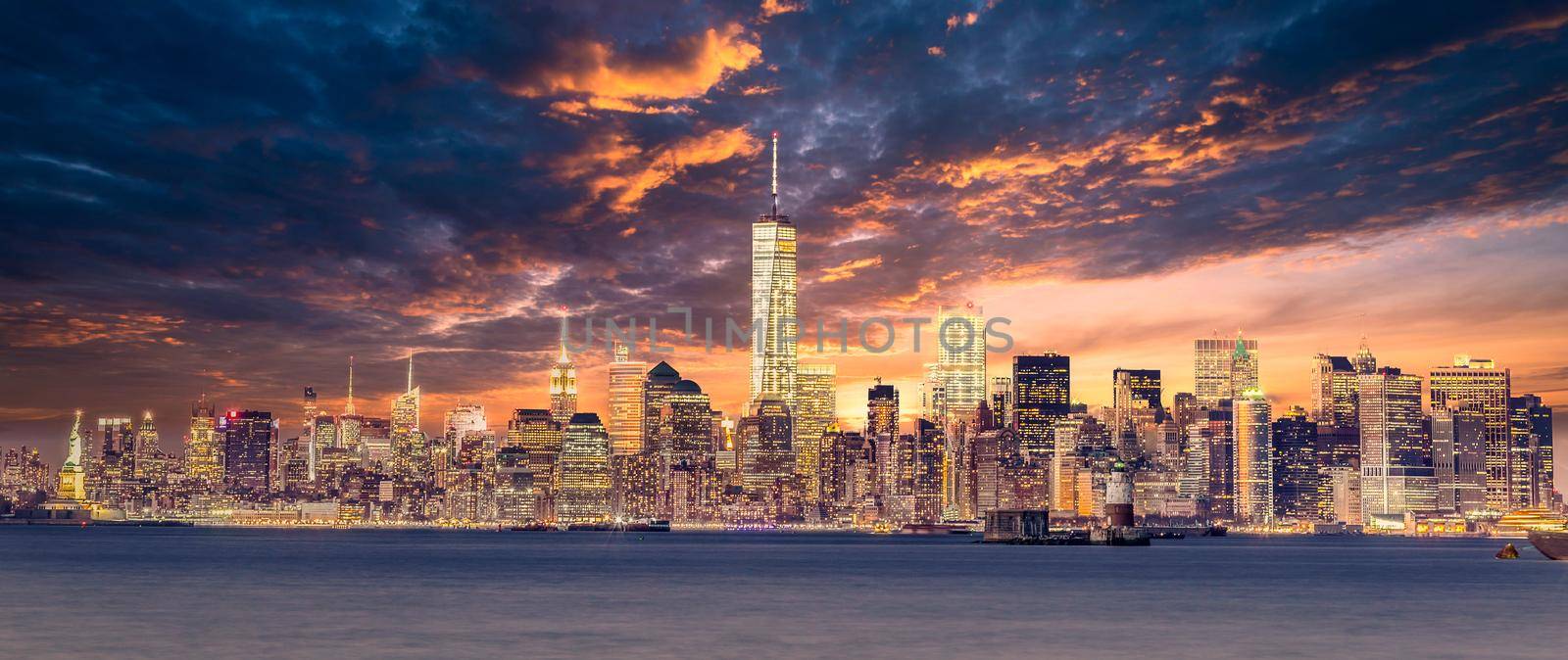 New York City Manhattan downtown skyline at dusk with skyscrapers illuminated over Hudson River panorama. Dramatic sunset sky. by kasto