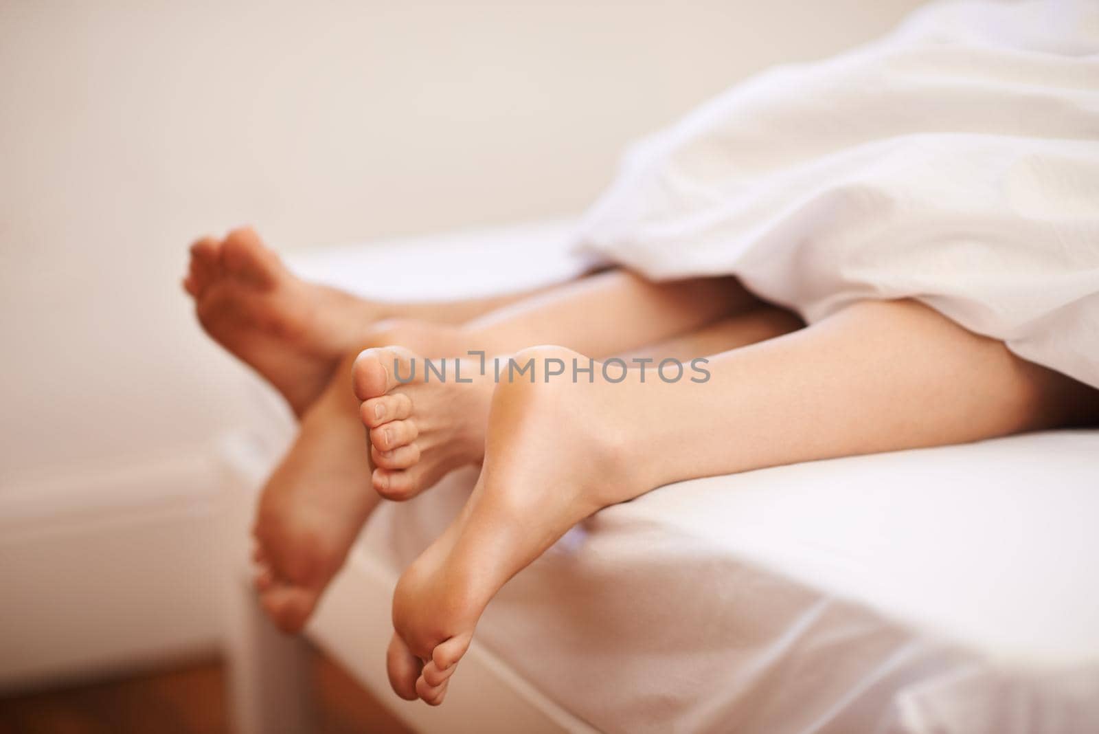 Cropped view of a couples feet as they lie in bed together.