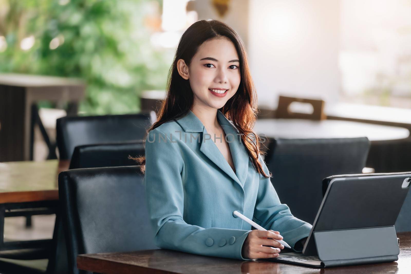 A female entrepreneur or businesswoman showing a smiling face while operating a computer tablet working on a wooden table. by Manastrong