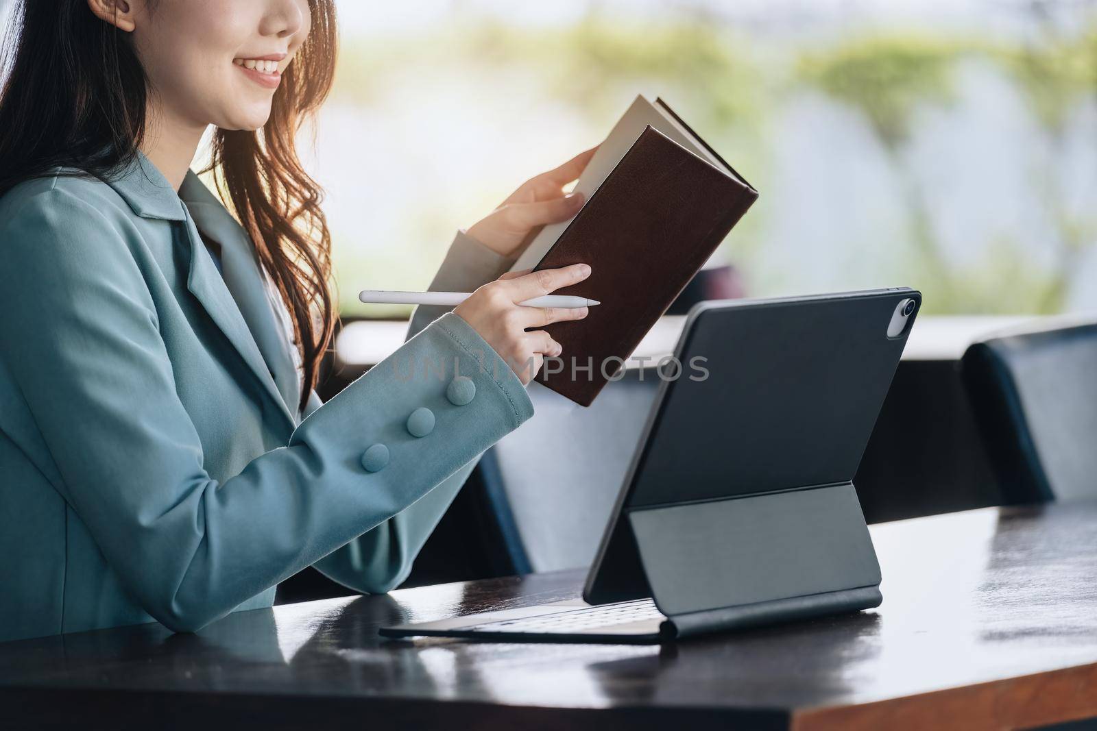 businesswoman showing a smiling face while reading a book developing financial and investing strategies and operating a computer tablet working on a wooden table