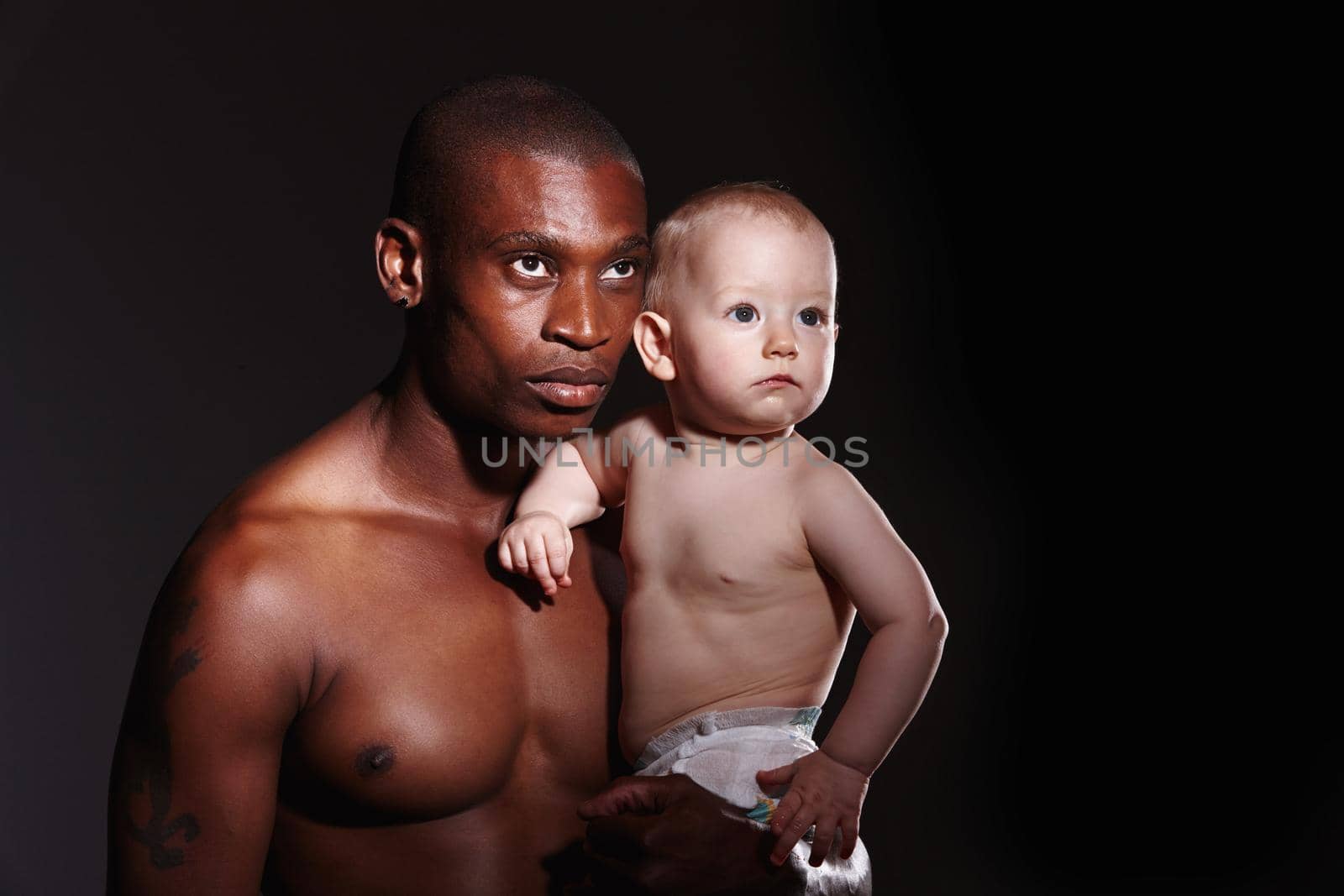 Concept shot of a man holding a little boy in his arms against a black background.