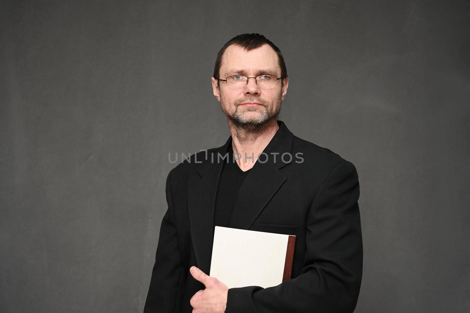 A businessman in a jacket looks at the camera with a folder in his hands. Portrait on a gray background in the studio