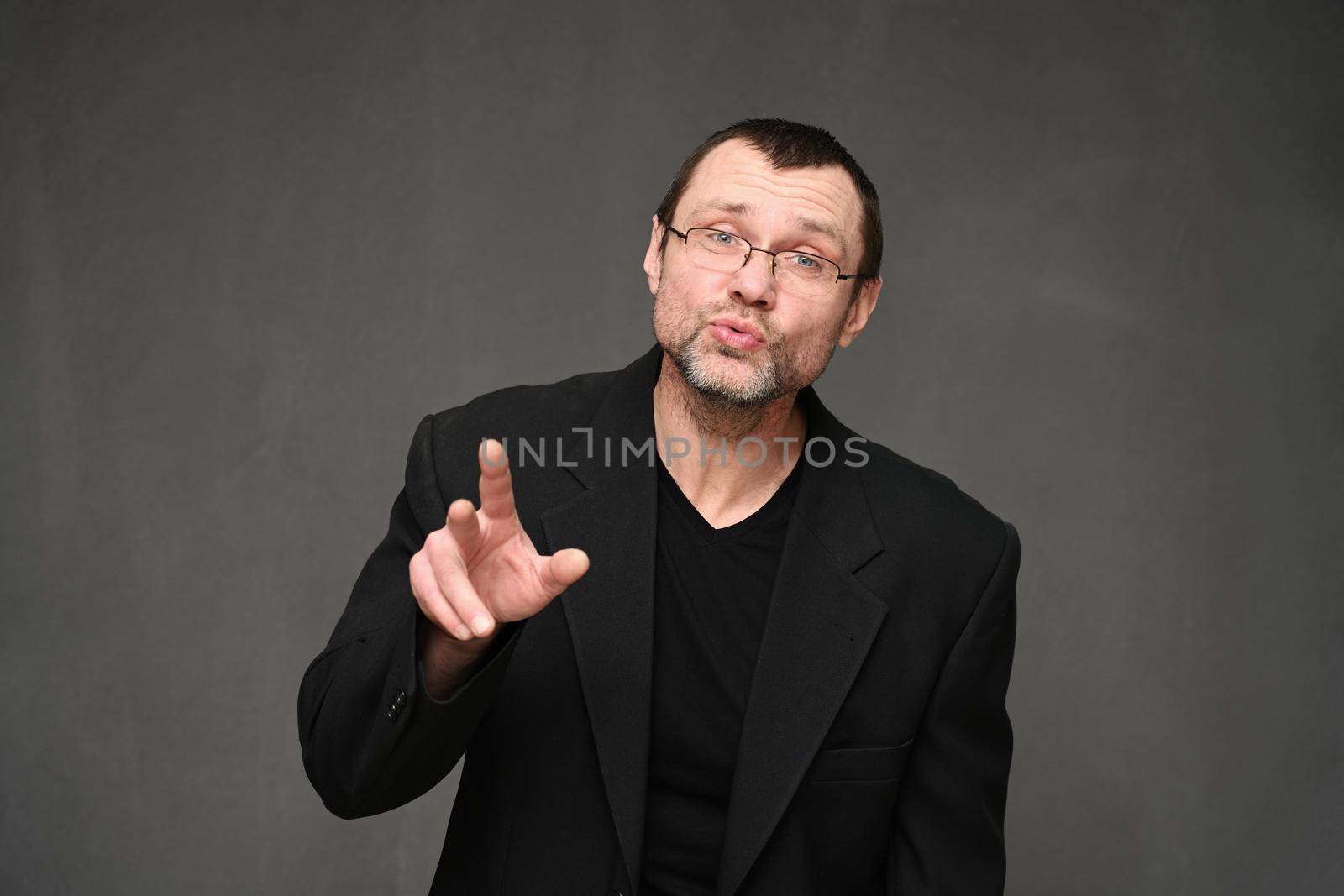 Businessman in a jacket and glasses with emotions talking to the camera. Portrait of an adult man on a gray background in the studio by chichaevstudio