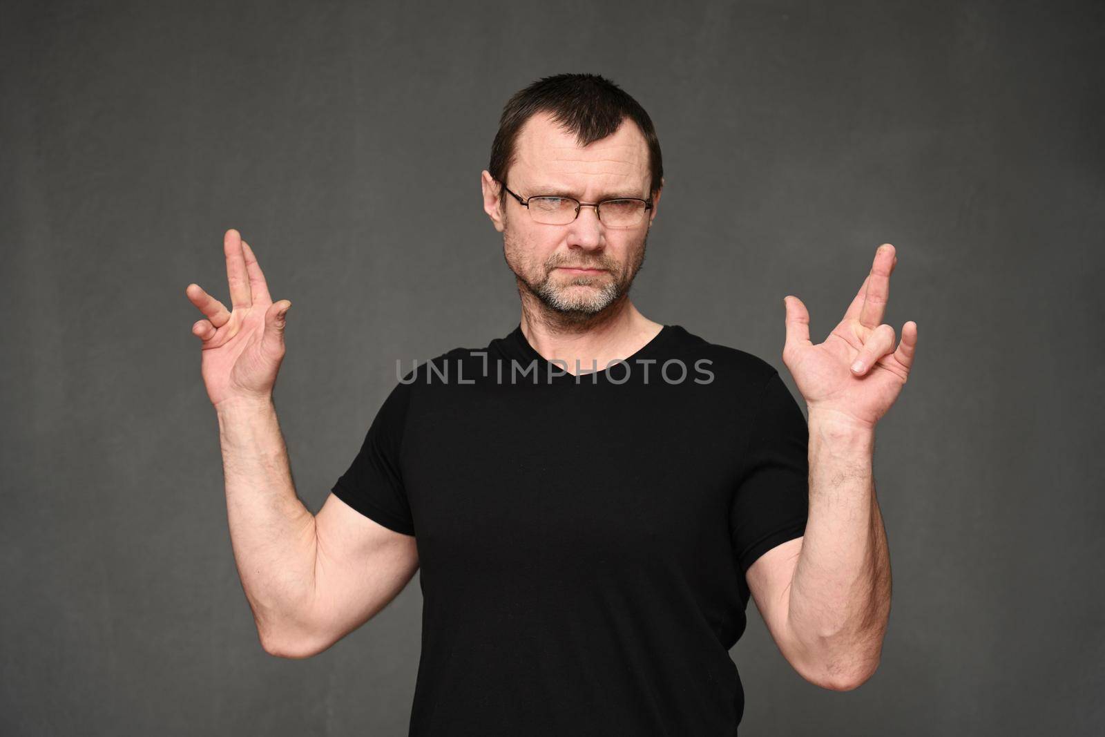 An adult man in glasses shows crossed fingers with a serious look.