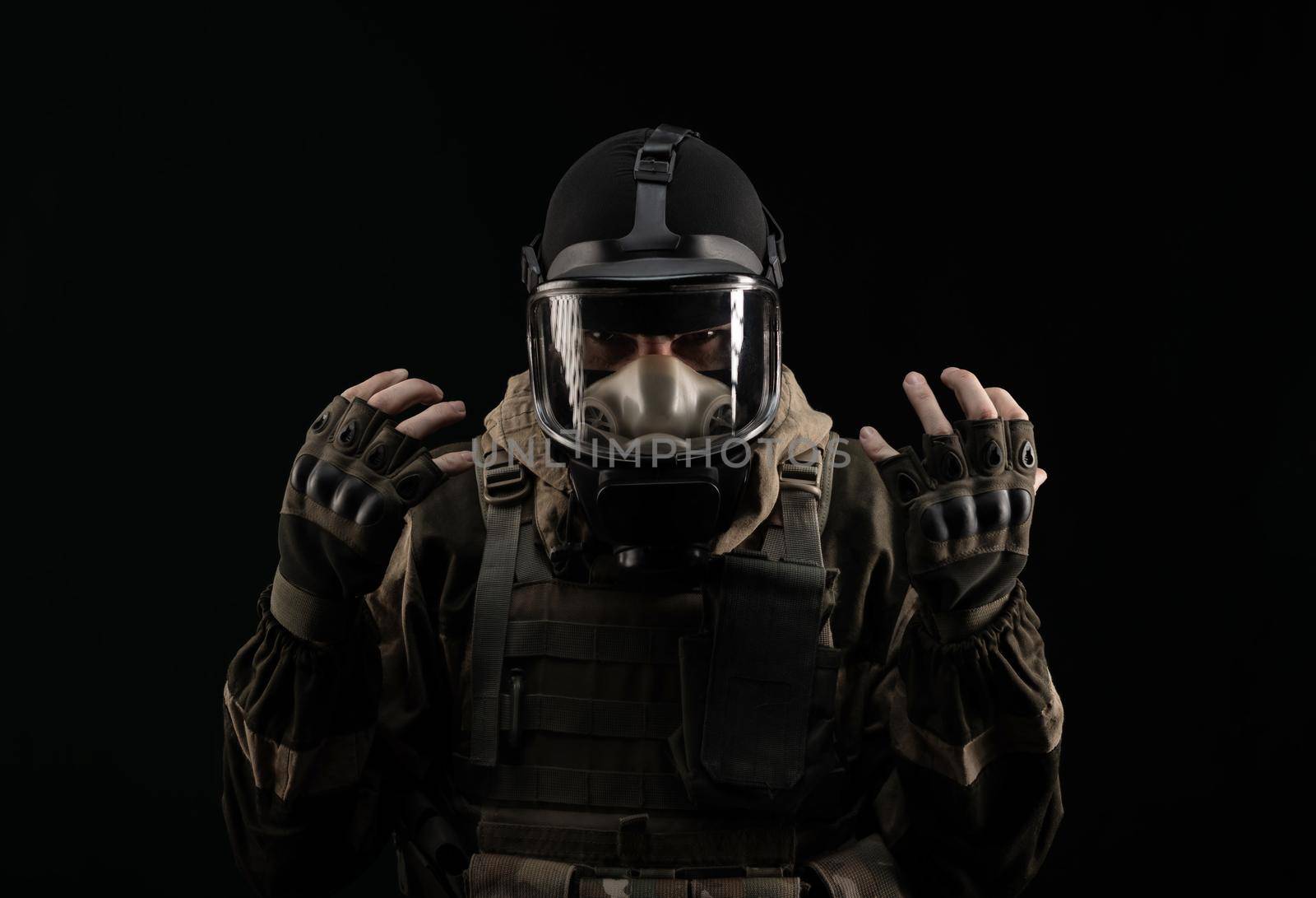 man in a military uniform and a gas mask holds with an angry expression of emotions on a black background