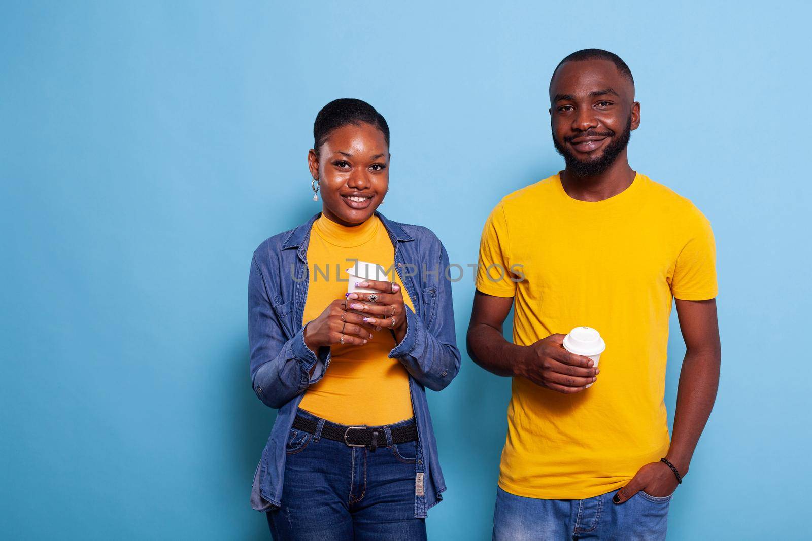 People in relationship smiling and holding cup of coffee in hand. Young couple enjoying hot beverage, expressing love feelings and looking at camera. Girlfriend and boyfriend in studio.