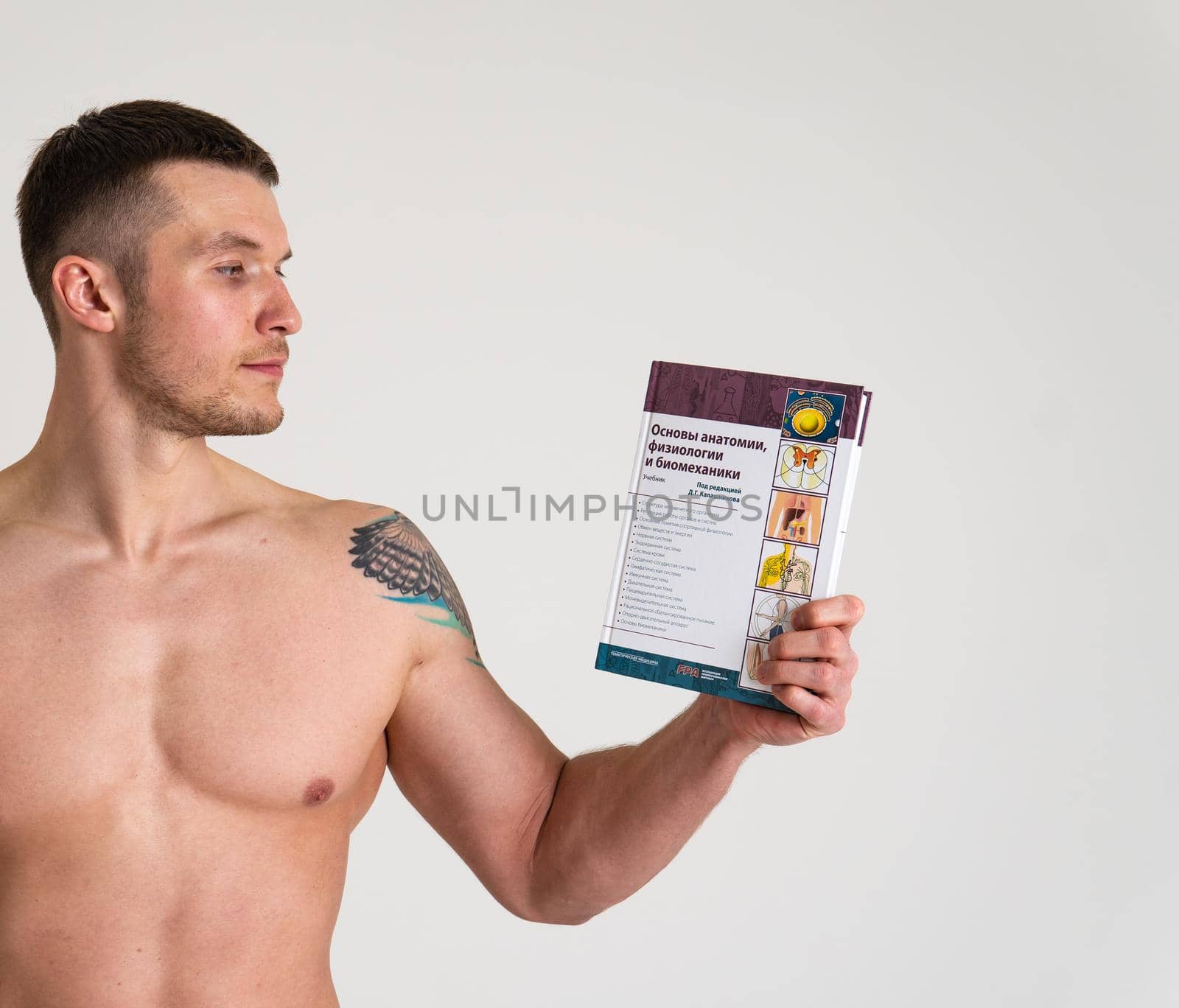 Bodybuilder reads the book on a white background isolated at the bottom of his head on his hands book athletic strong person body healthy, standing. Health ABS gym, strength tan