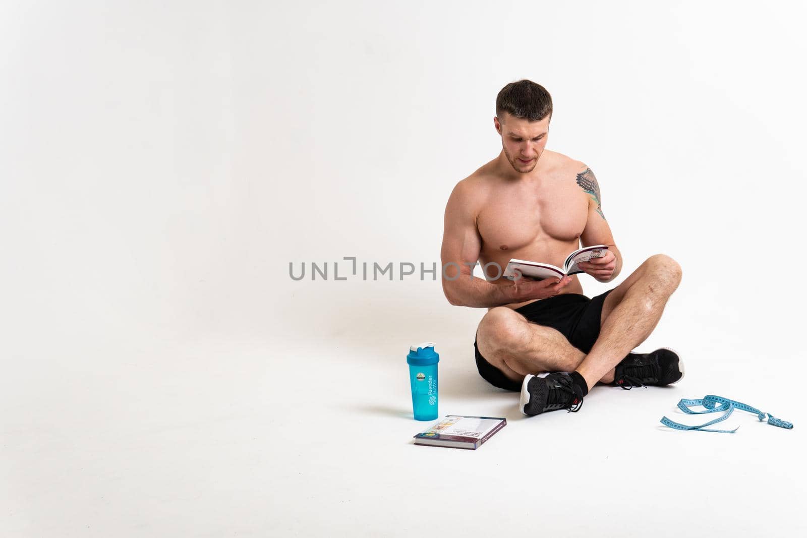Bodybuilder reads the book on a white background isolated at the bottom of his head on his hands male young muscular, white guy shirtless, sexy sport. biceps, strength tan