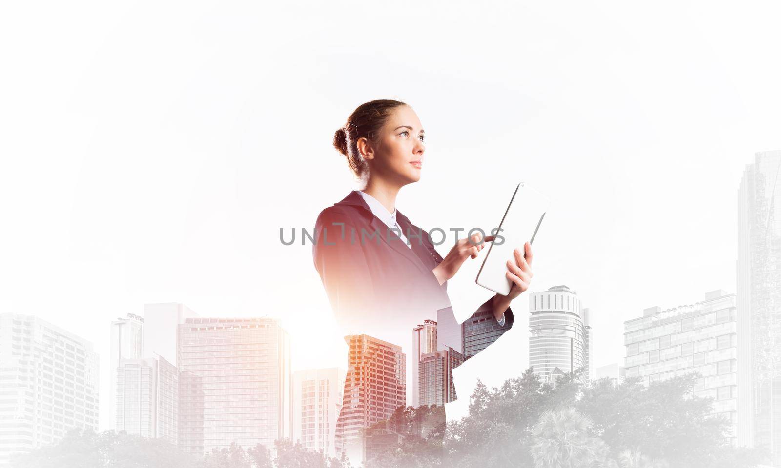 Young businesswoman with tablet computer on modern cityscape background. Double exposure concept with beautiful woman in business suit. Digital technology in stock trading and real estate investment