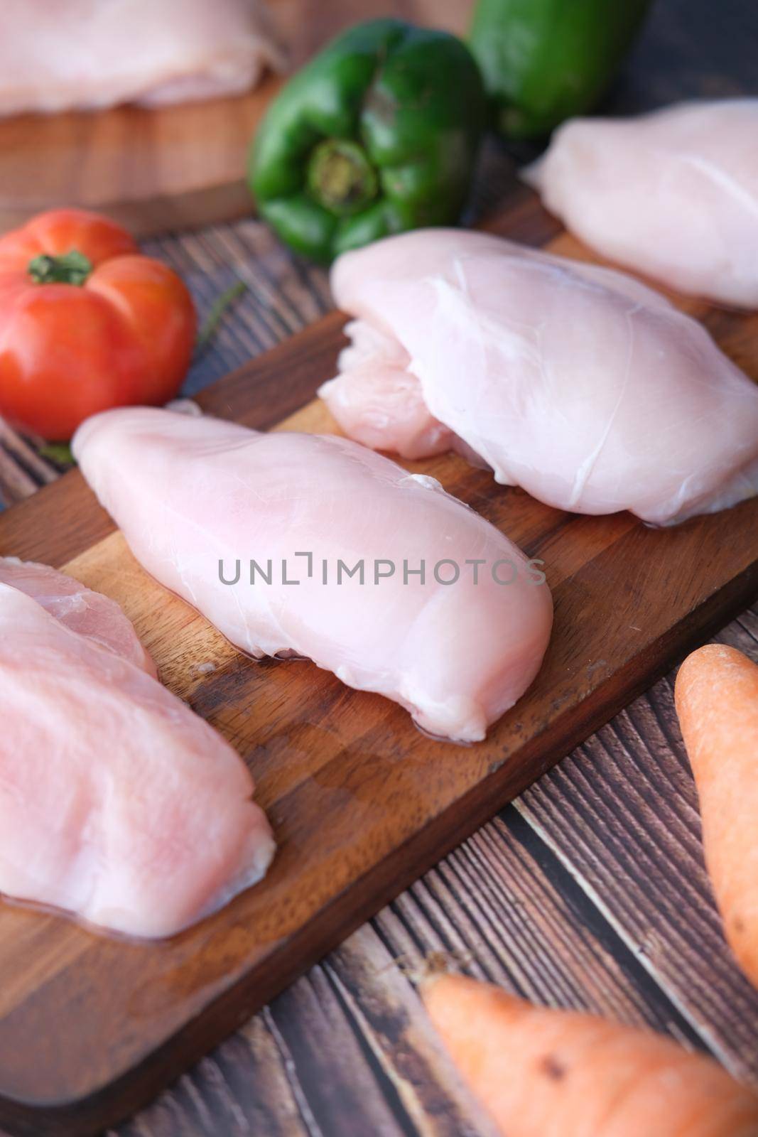 top view of raw chicken breast on a chopping board with vegetables on table ,