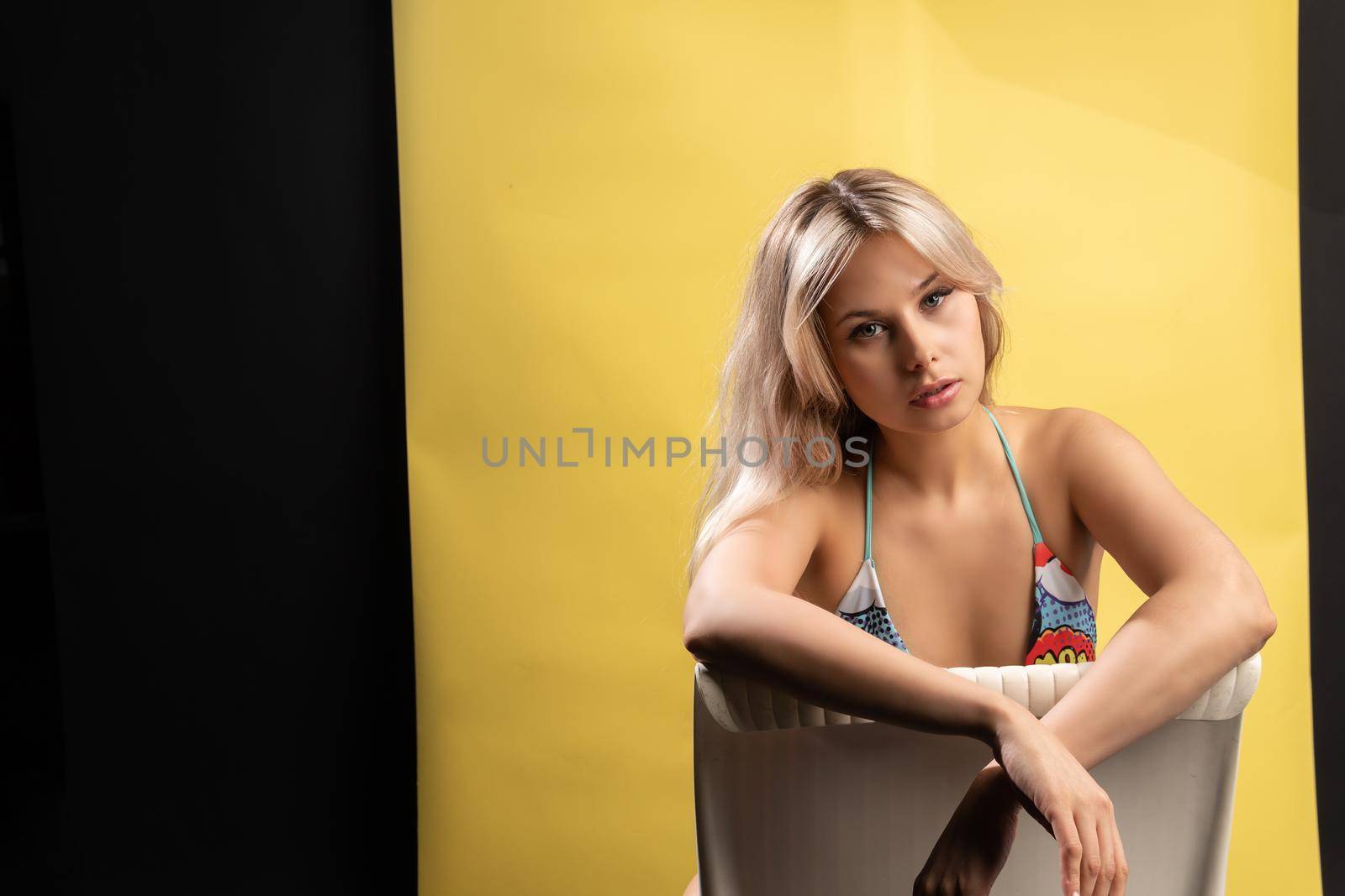 A girl sits on a chair in a swimsuit on a yellow background a beautiful smiles to have fun beautiful swimsuit swimwear, body beauty slim sport wear. Ass smiling bra chair