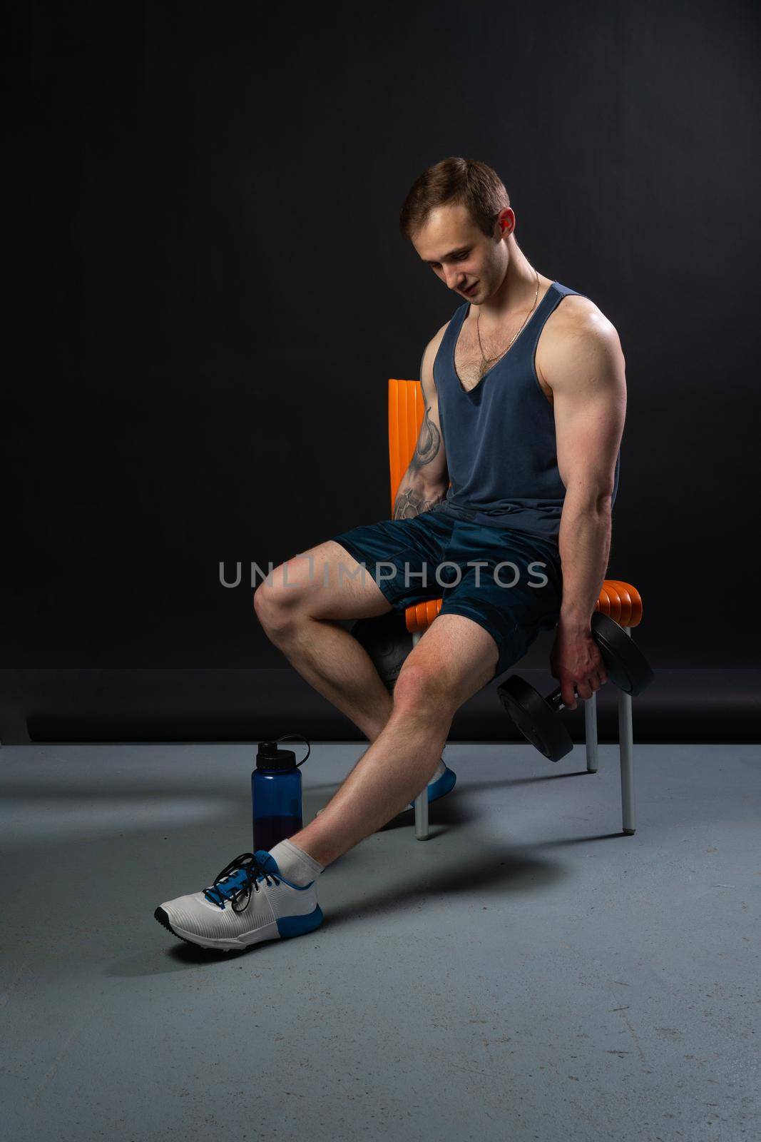 Man on black background keeps dumbbells pumped up in fitness bodybuilding sexy torso, arm exercise hold person weightlifting. Lift sportive metal, human fit sitting on a chair resting after a workout