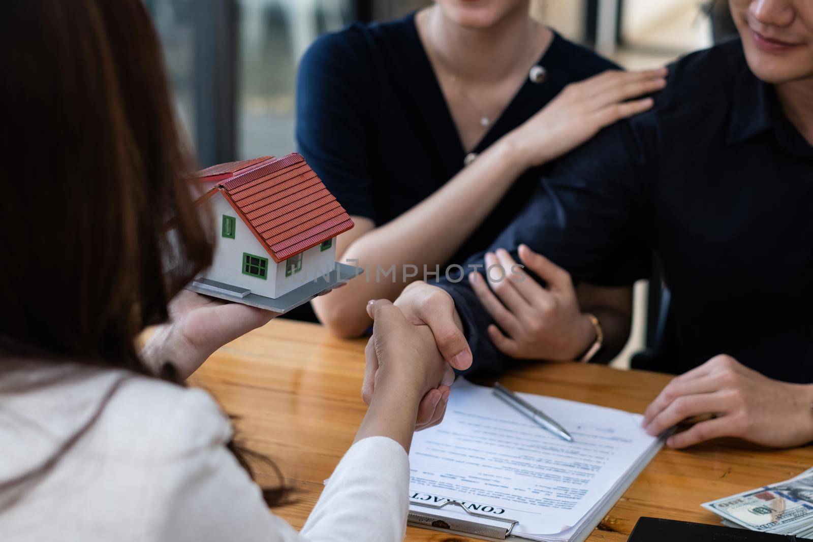 A happy young couple receives a wonderful bargain after signing a contract to purchase a home. Broker and customer shake hand after have a good deal. Real Estate concept