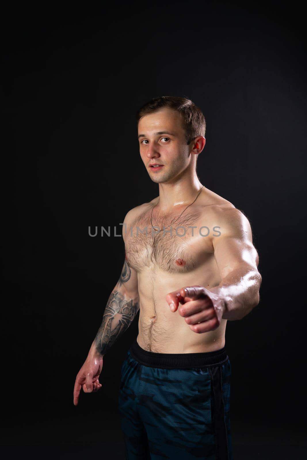 Man on black background keeps dumbbells pumped up in fitness bodybuilding biceps body muscular fitness bodybuilder powerful, shirtless weightlifting. handsome guy fit strains the presbytery muscles fingers point at us