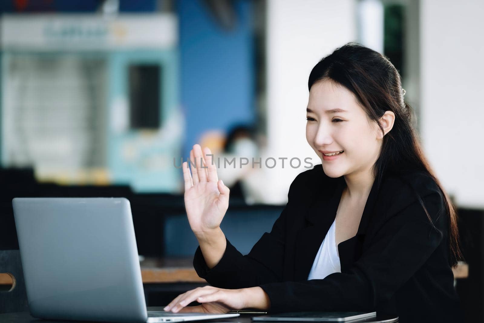 An Asian female employee or businessman is smiling and waving to a colleague using a notebook computer via video conferencing