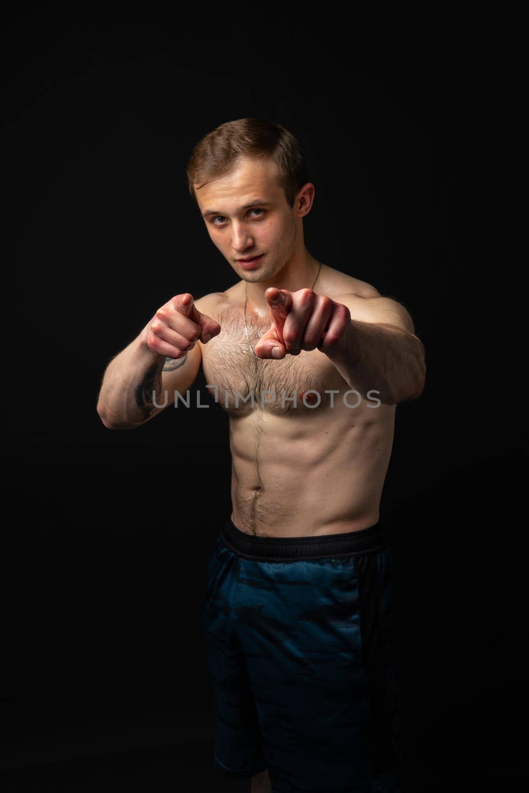 Man on black background keeps dumbbells pumped up in fitness active biceps black, fitness hold dumbbell, Young handsome adult, guy fit fingers point at us