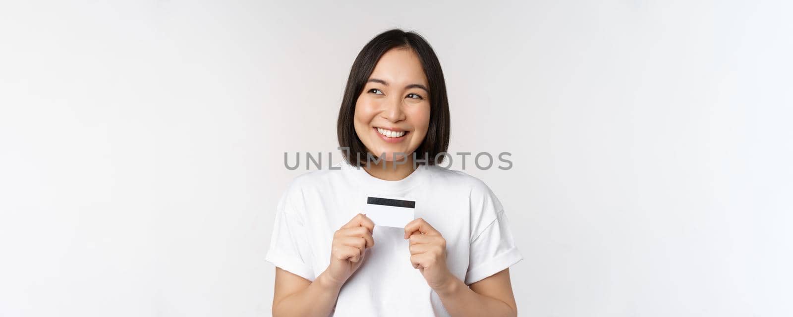 Smiling korean woman showing credit card with happy face, standing in tshirt over white background. Copy space