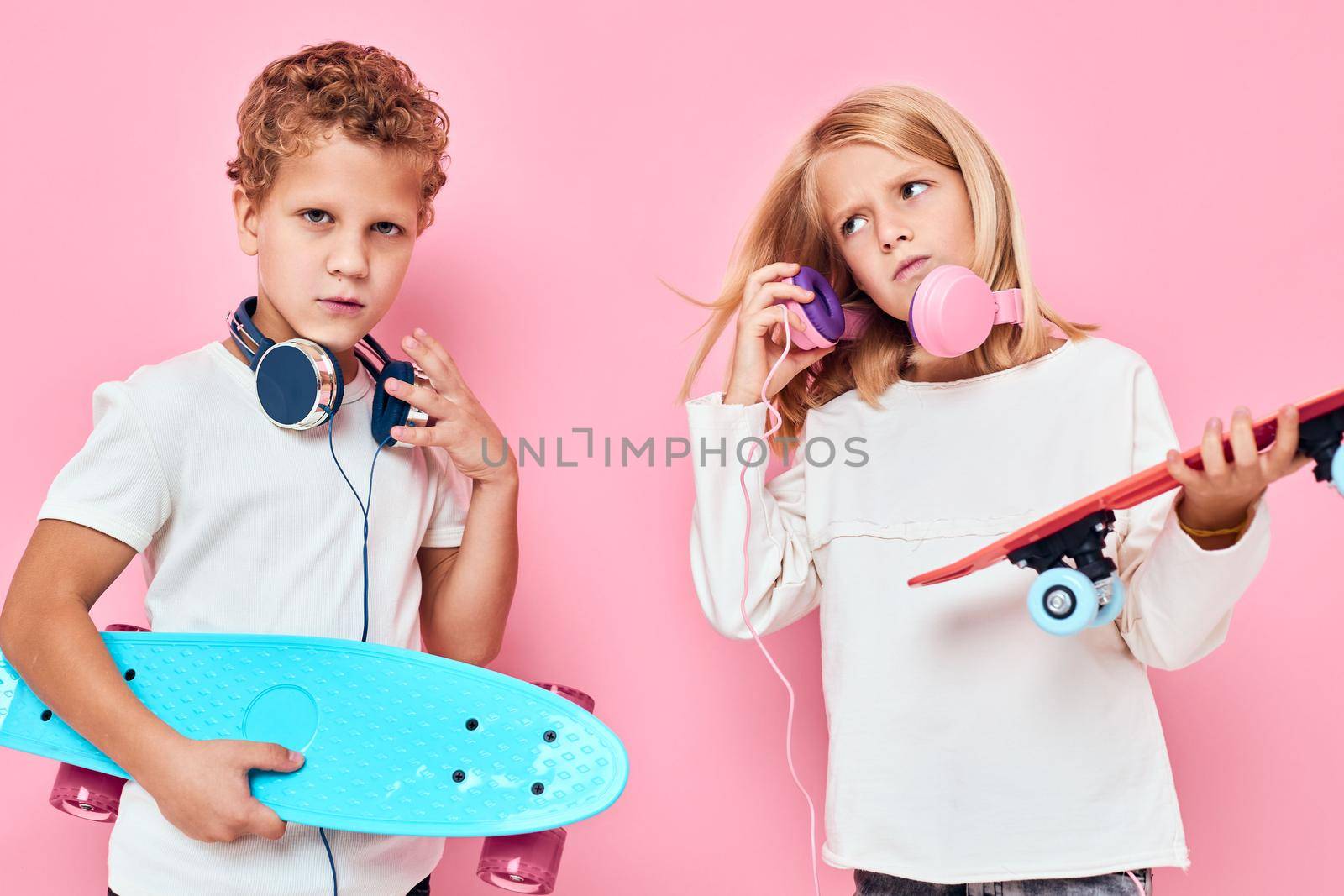 Funny children in headphones skateboards in hands pink color background. High quality photo