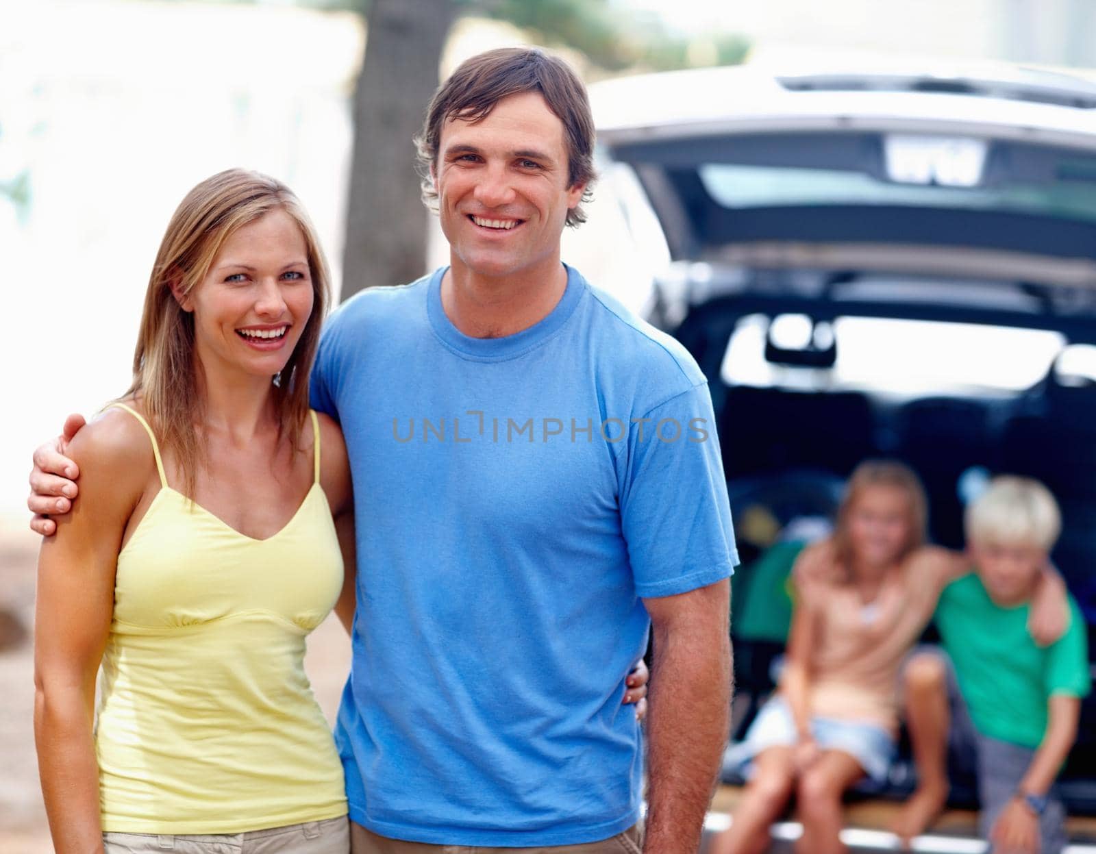 Portrait of couple smiling with kids sitting in the back of a car.