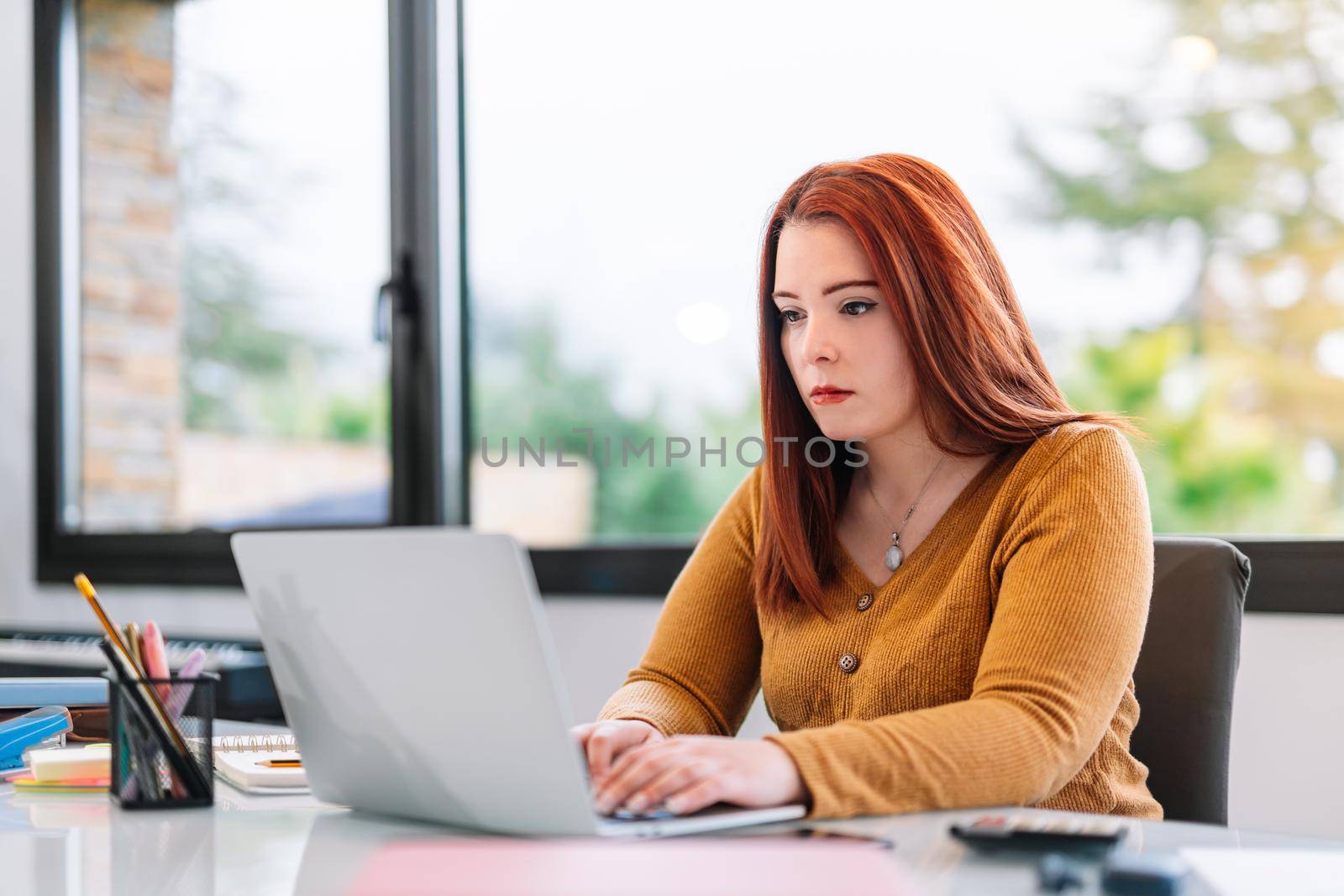 Young woman working on laptop from home by CatPhotography