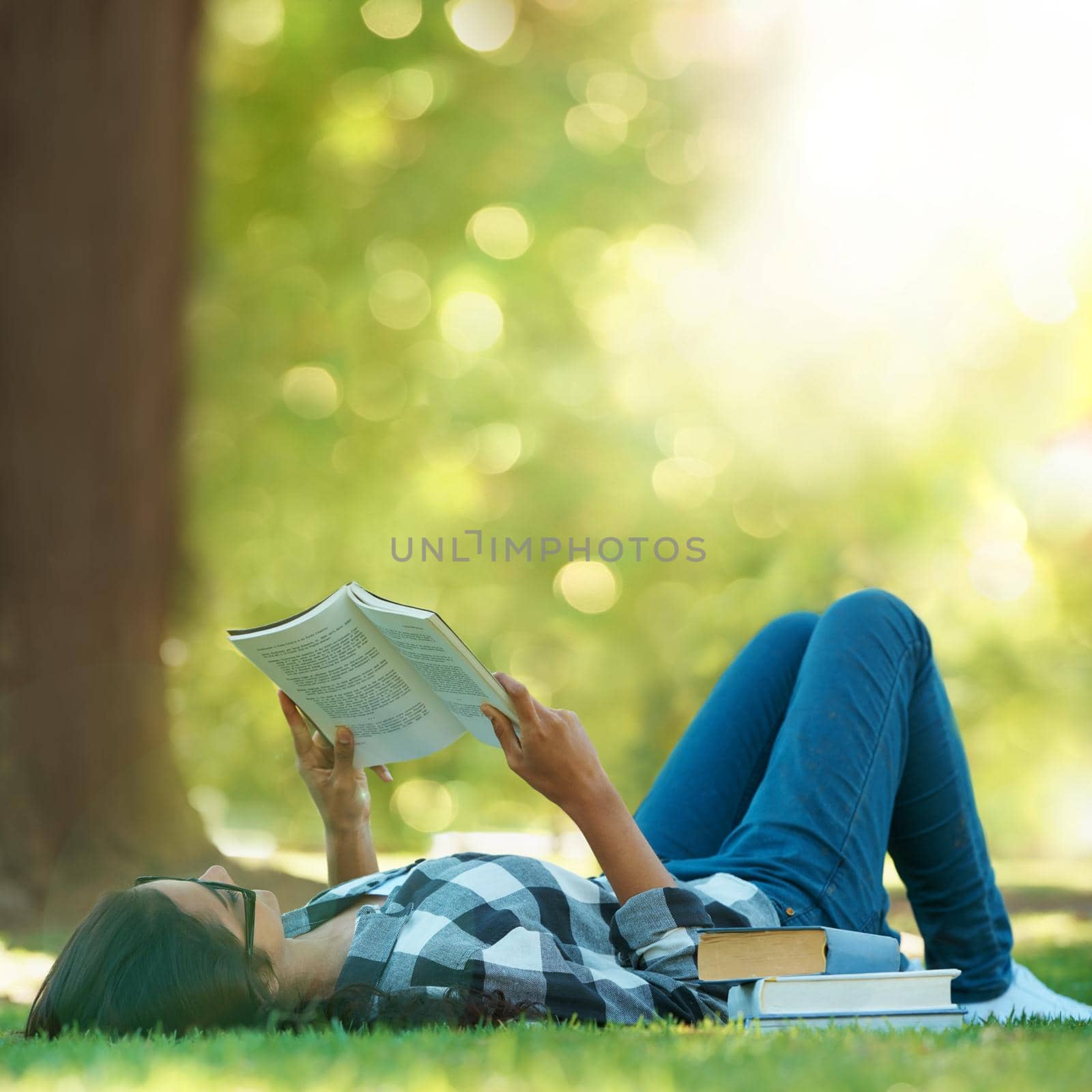 Shot of a young woman lying on grass and reading a book.