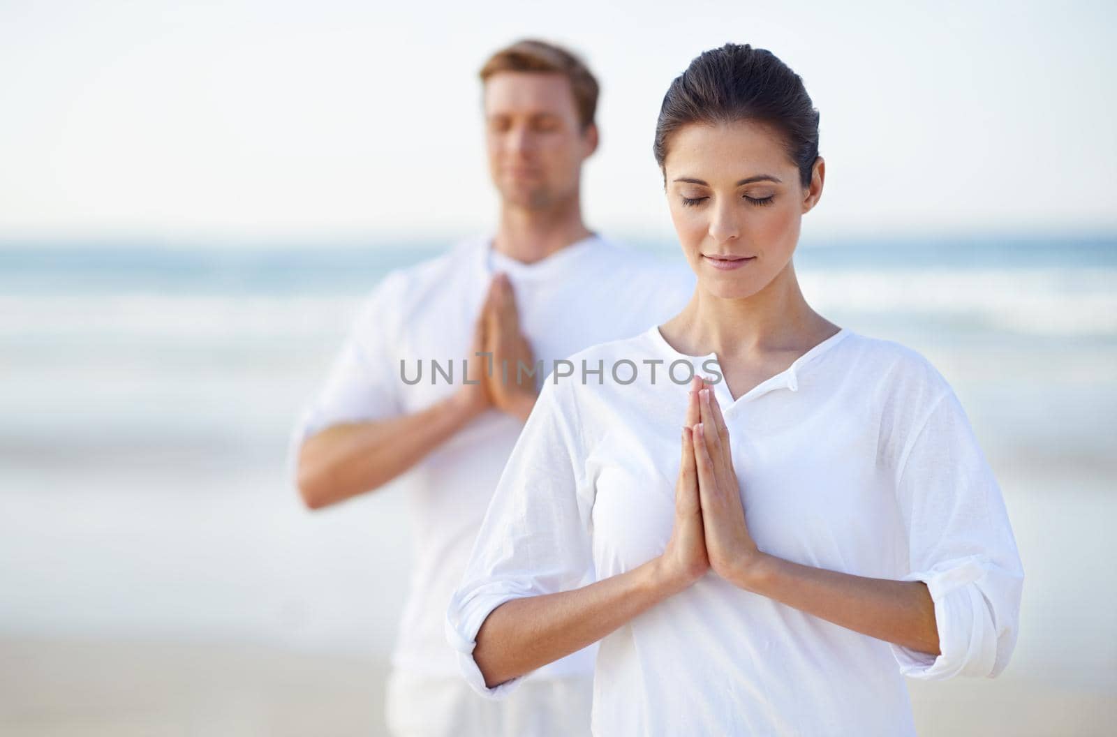 A young couple practising yoga on the beach.