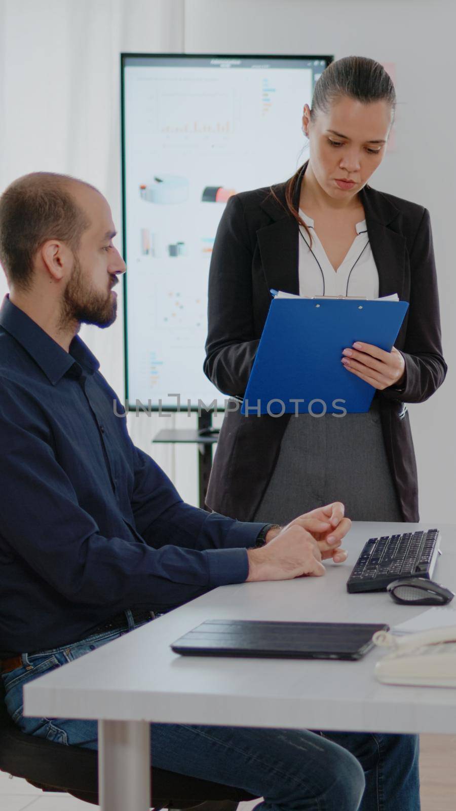 Colleagues working together on business development with computer and presentation papers. Workmates using technology for marketing development and strategy planning at corporate job.