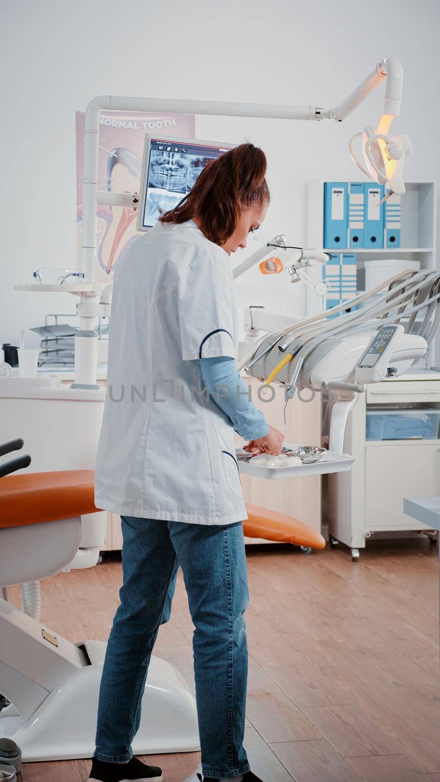 Vertical video: Woman dentist preparing stomatology chair and equipment for oral care and dental examination in cabinet. Teethcare specialist working with dentistry tools for checkup