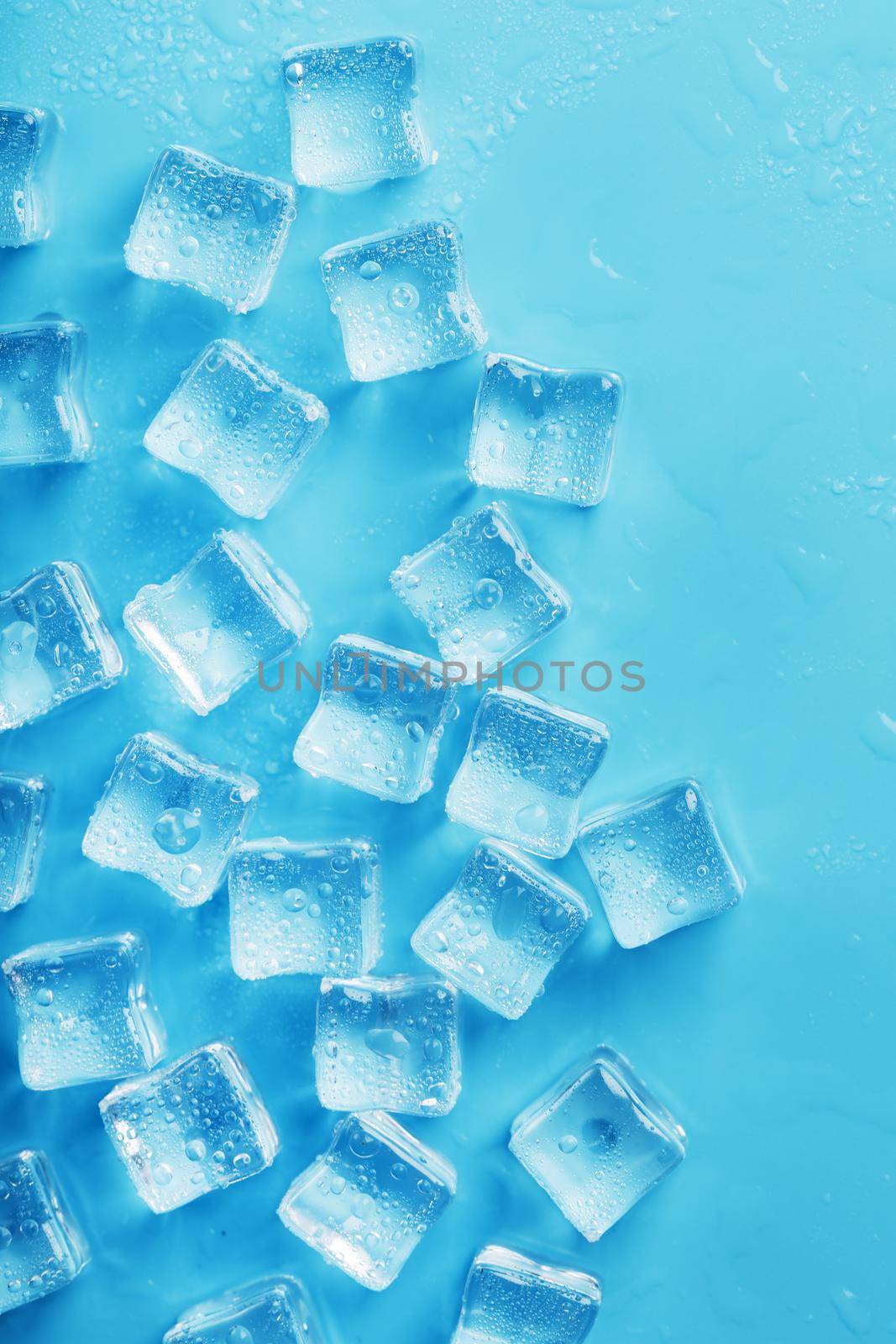 Ice cubes with water drops scattered on a blue background, top view. Refreshing ice.