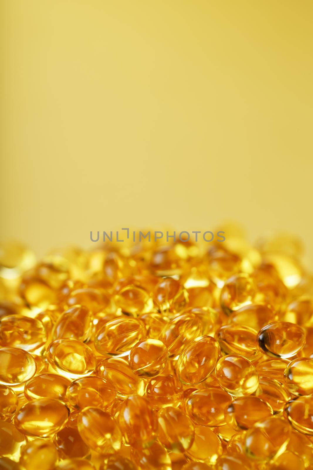 Pile of golden capsules of vitamin D3 on a yellow background with free space. Biologically active substances of the calciferol group are fat-soluble organic compounds.