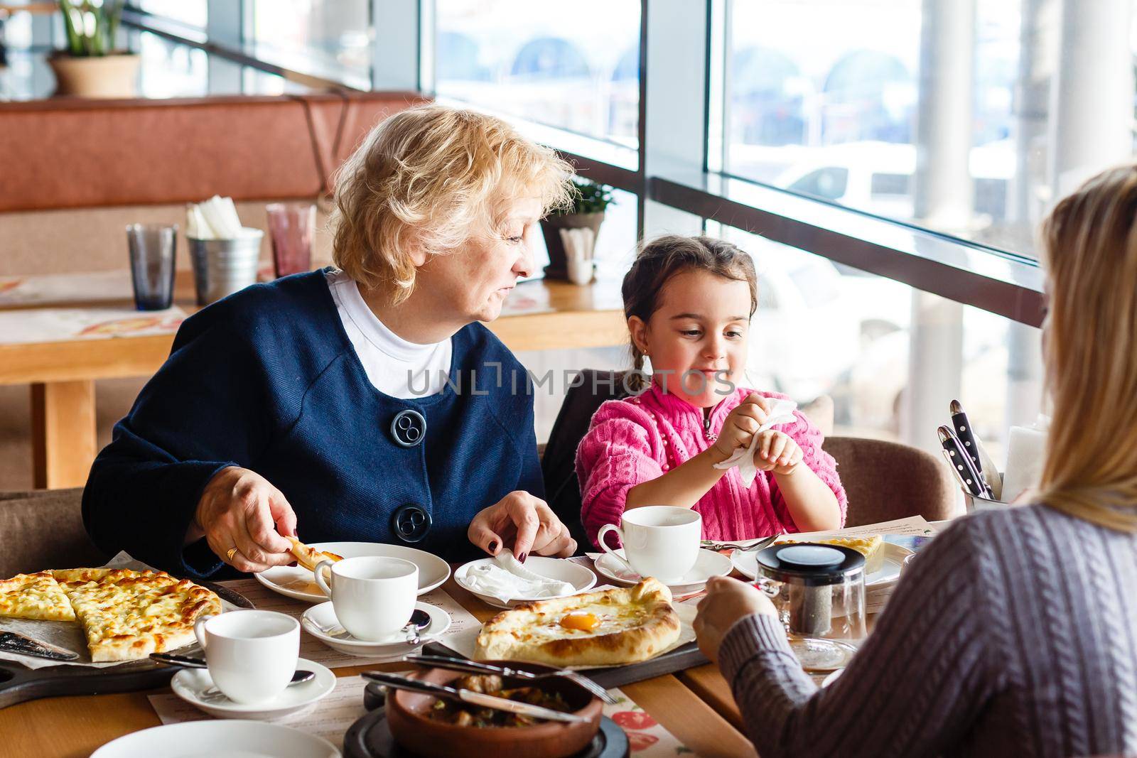 childhood and people concept - happy grandmother and little girl with spoon eating at outdoor cafe or restaurant