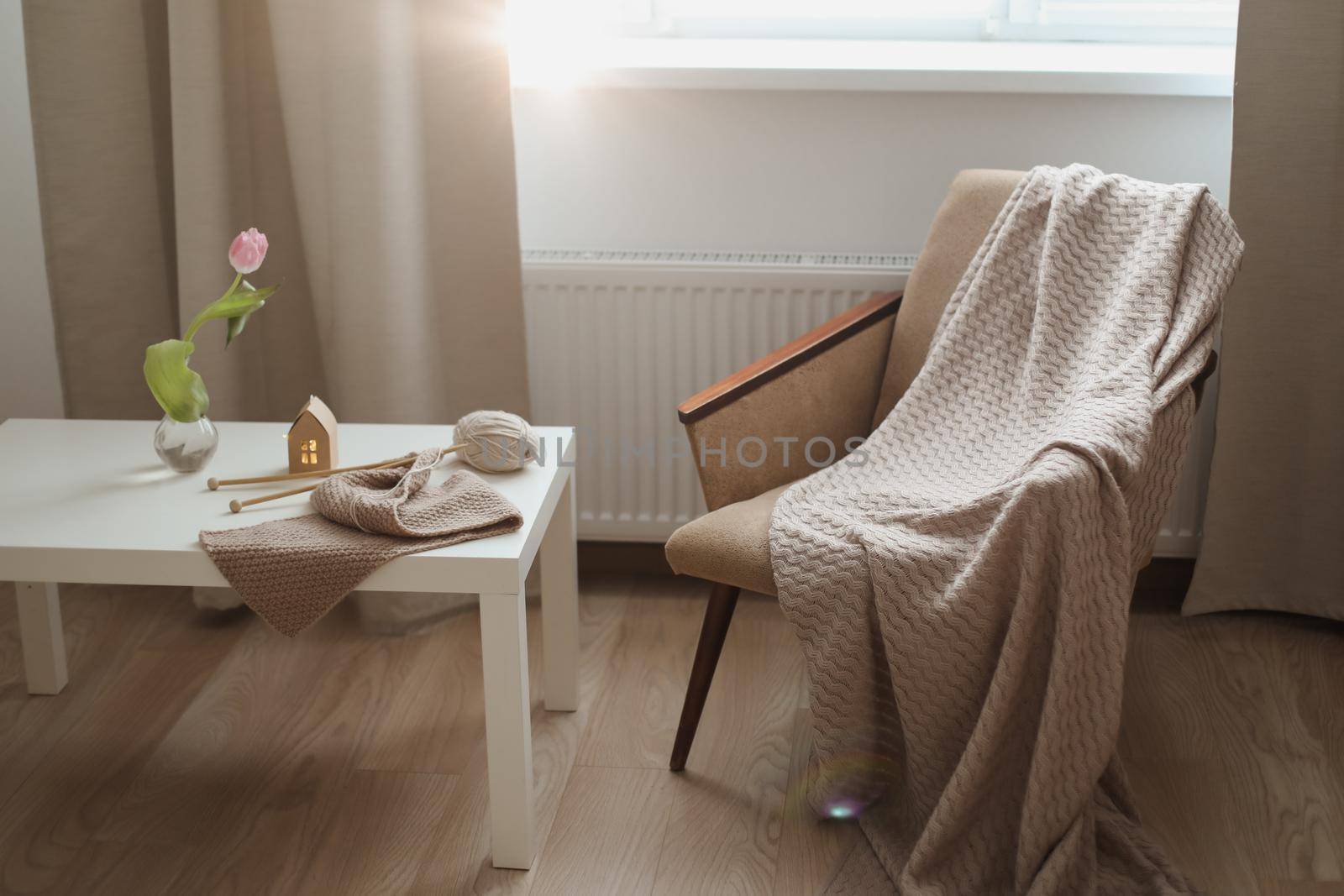 cozy home interior decor with a chair, plaid, table and knitting needles with threads, beige yarn.