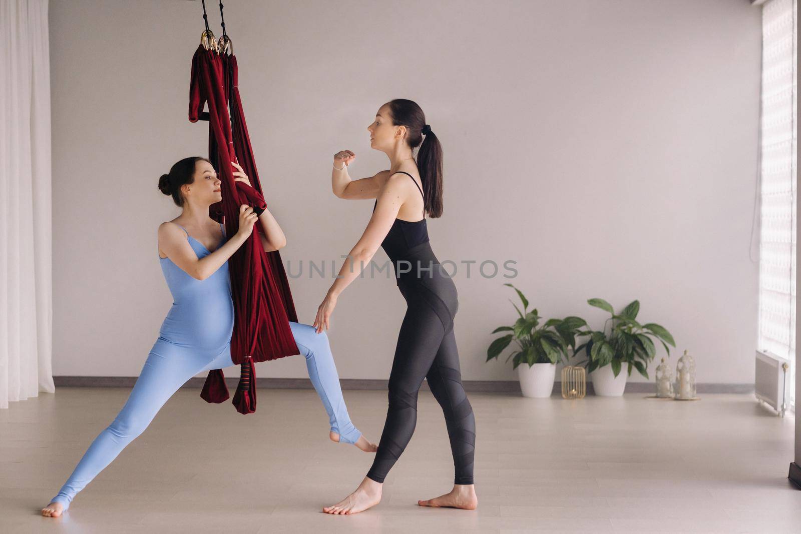 Pregnant girl. A woman with a trainer does yoga in a hammock in the gym. The concept of a healthy lifestyle, motherhood.