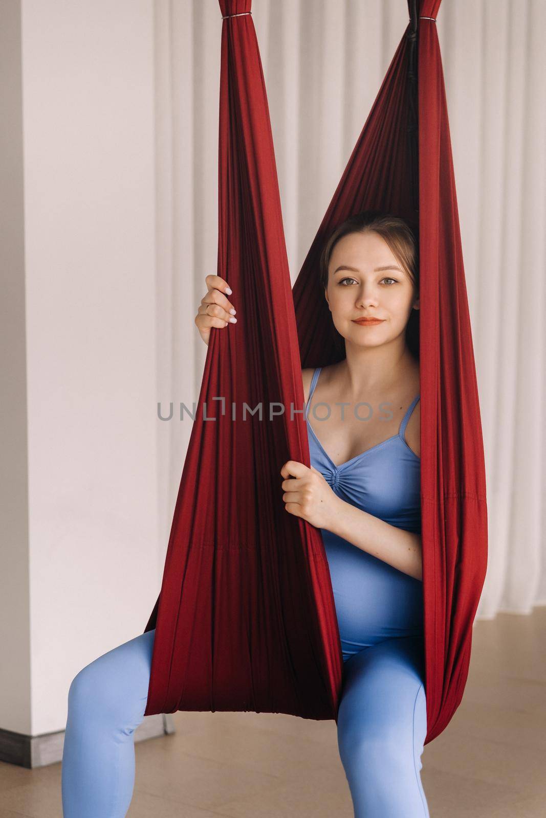 Pregnant girl. A woman does yoga sitting in a hammock in the gym. The concept of a healthy lifestyle, motherhood.