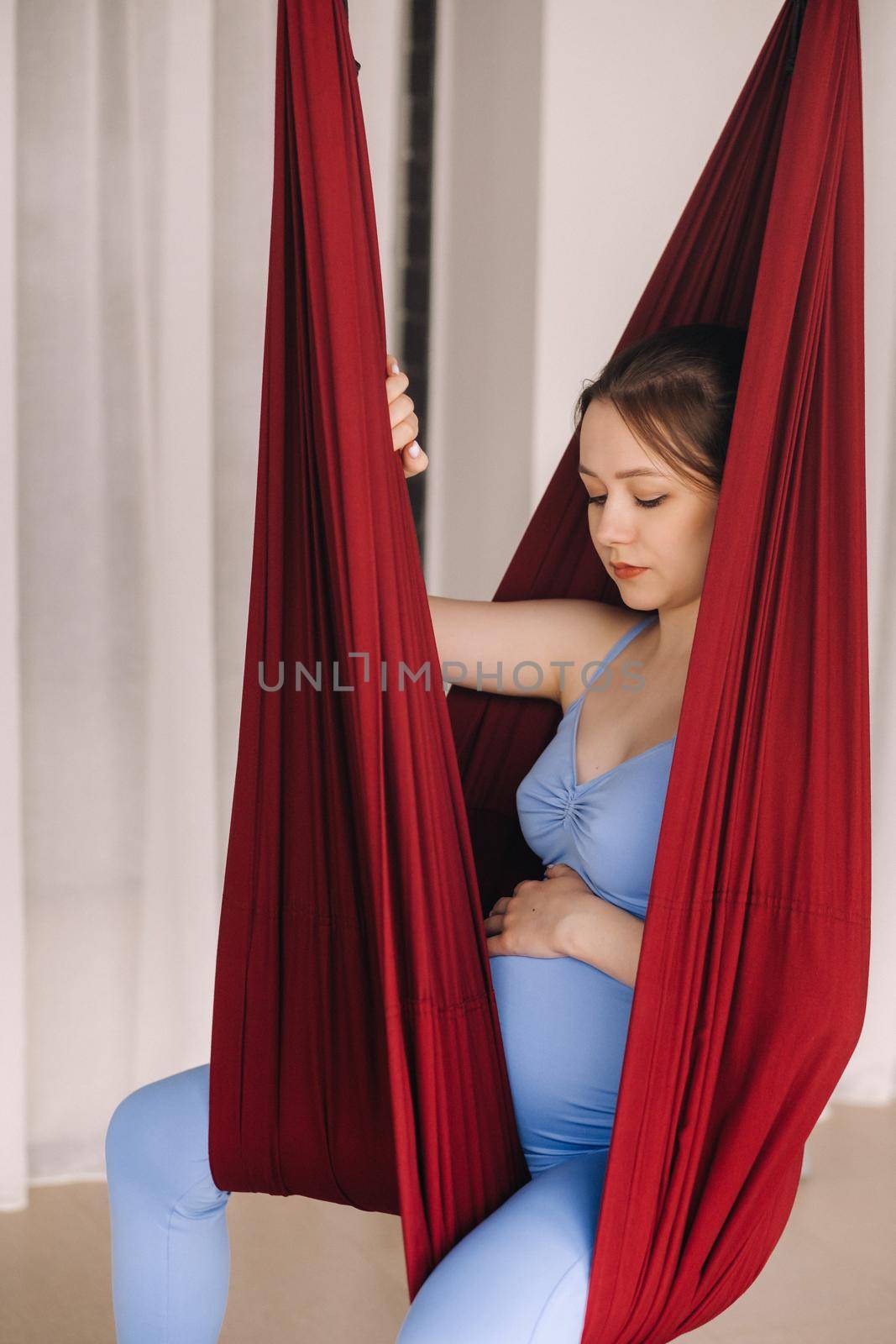 Pregnant girl. A woman does yoga sitting in a hammock in the gym. The concept of a healthy lifestyle, motherhood.