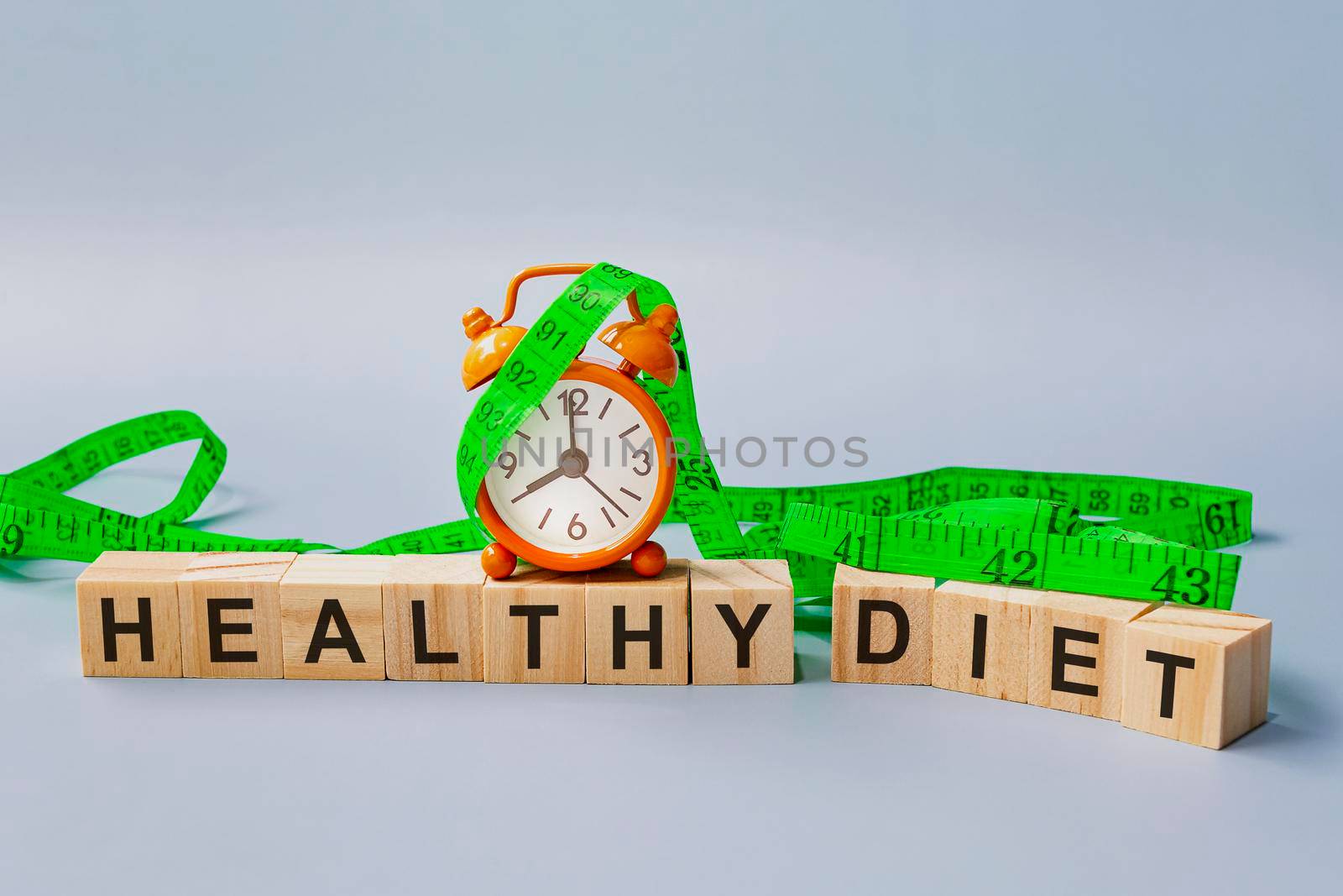 Healthy diet text on wooden block cube with measure tap and orange clock on blue background. Alarm set at 8 o'clock. Diet concept.