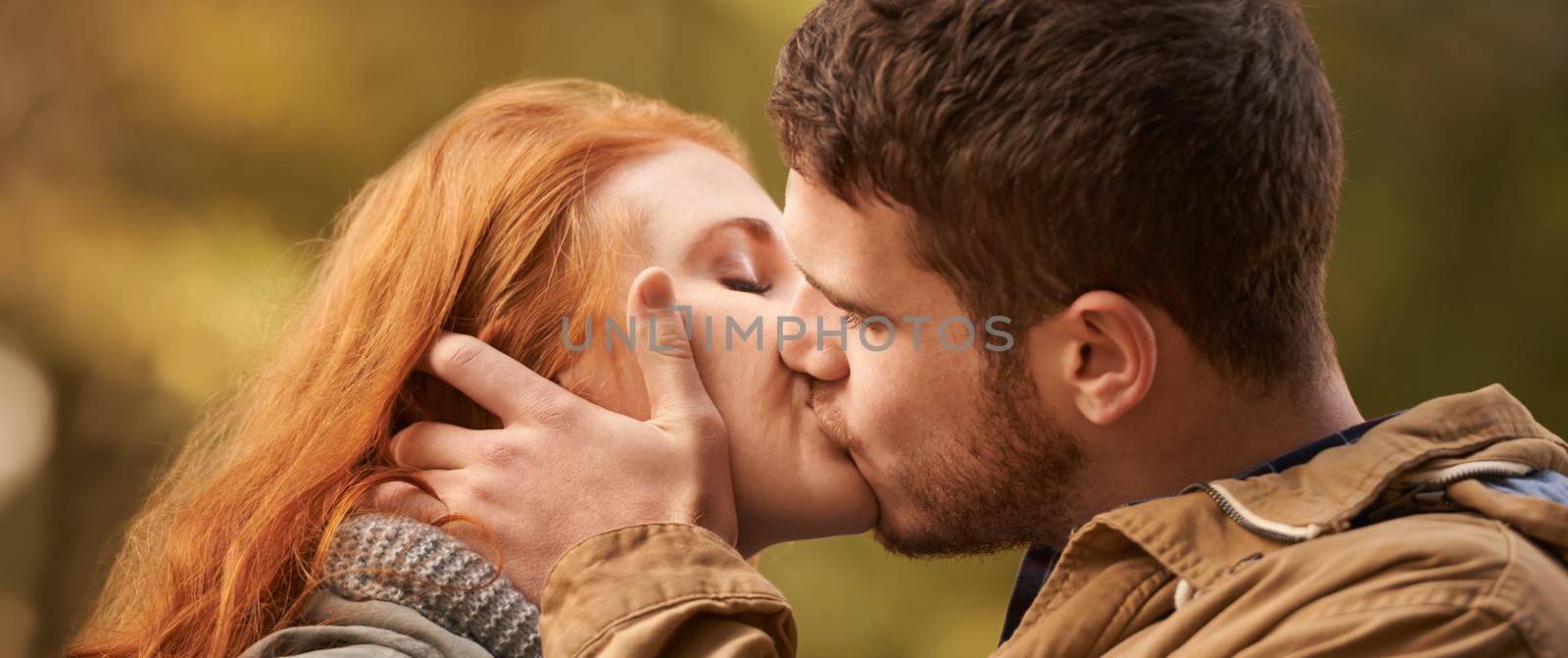 Kiss me like you miss me. Shot of a happy young couple sharing a kiss outdoors. by YuriArcurs