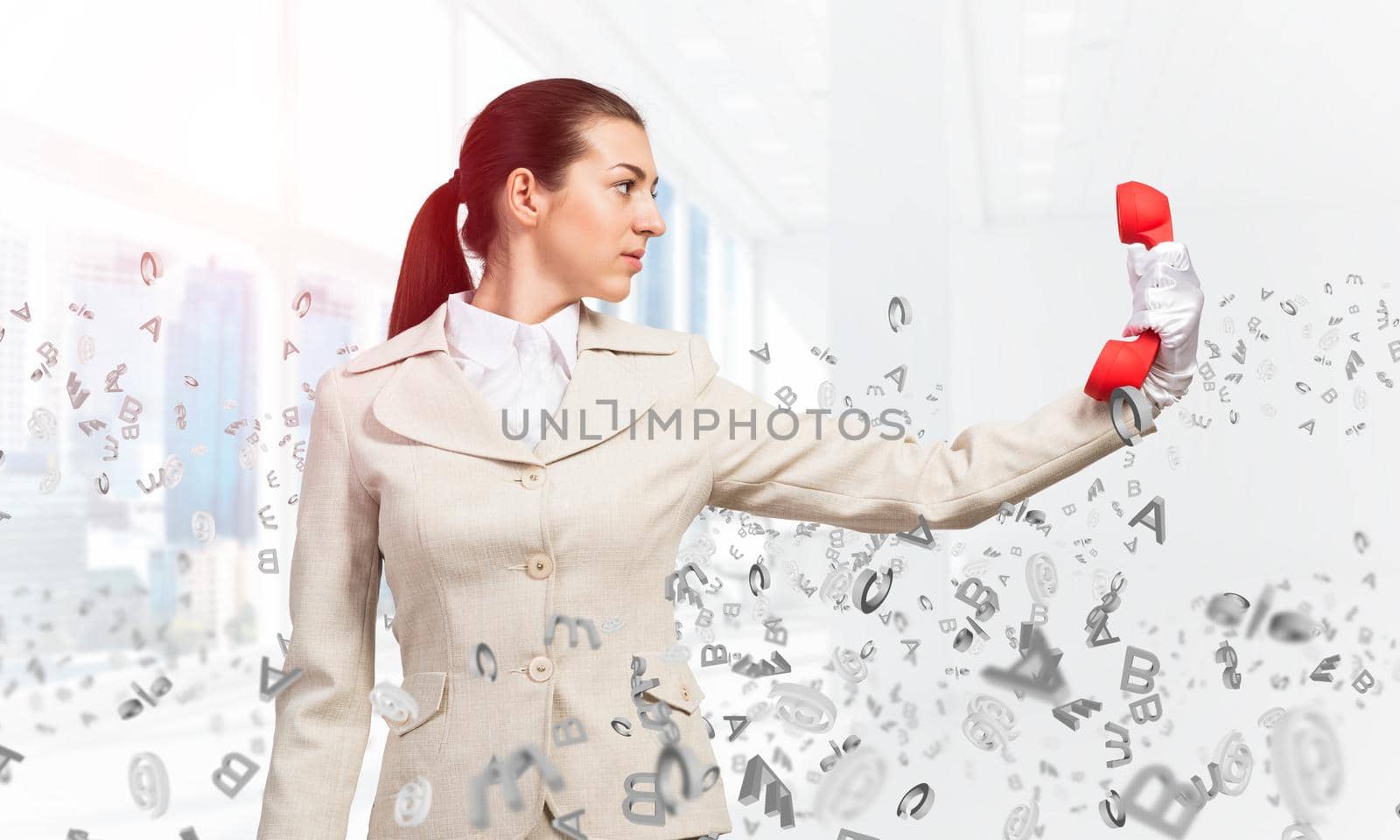 Woman keep at distance vintage red phone. Elegant operator in white business suit posing with landline phone in office with flying various letters. Hotline telemarketing and business communication.