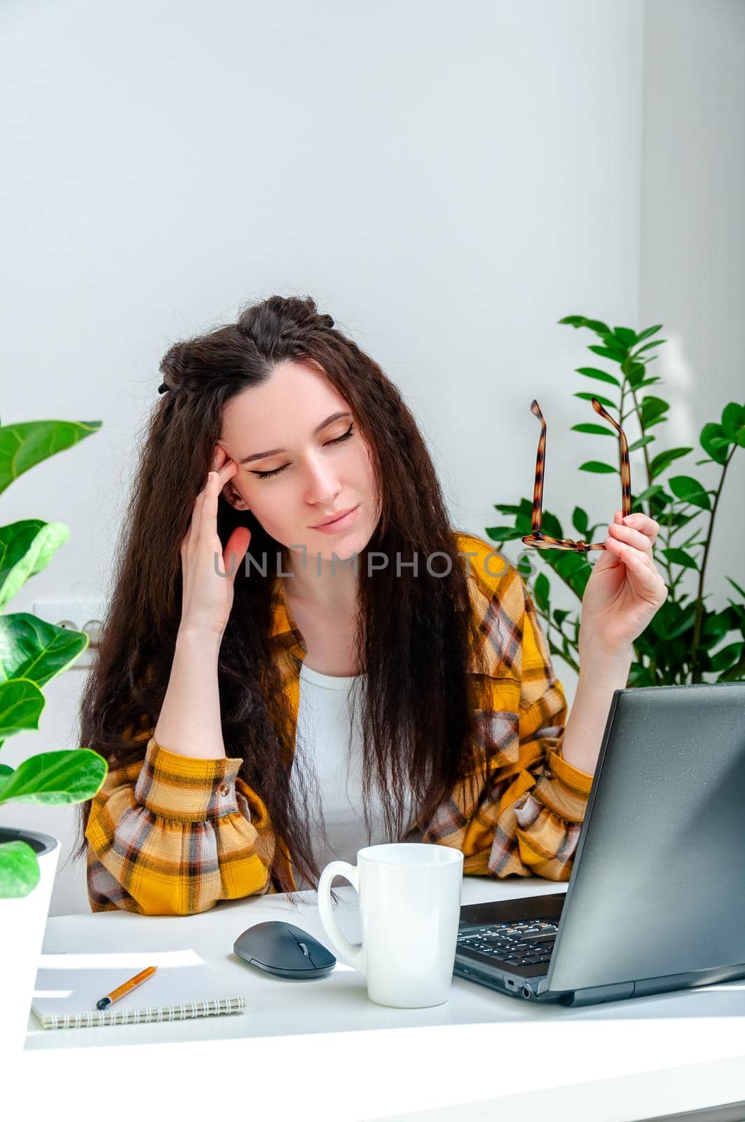 Beautiful woman holds her temples because of a headache or eye pain from working at a laptop. Woman working at home, undergoing training, watching webinar, online shopping.