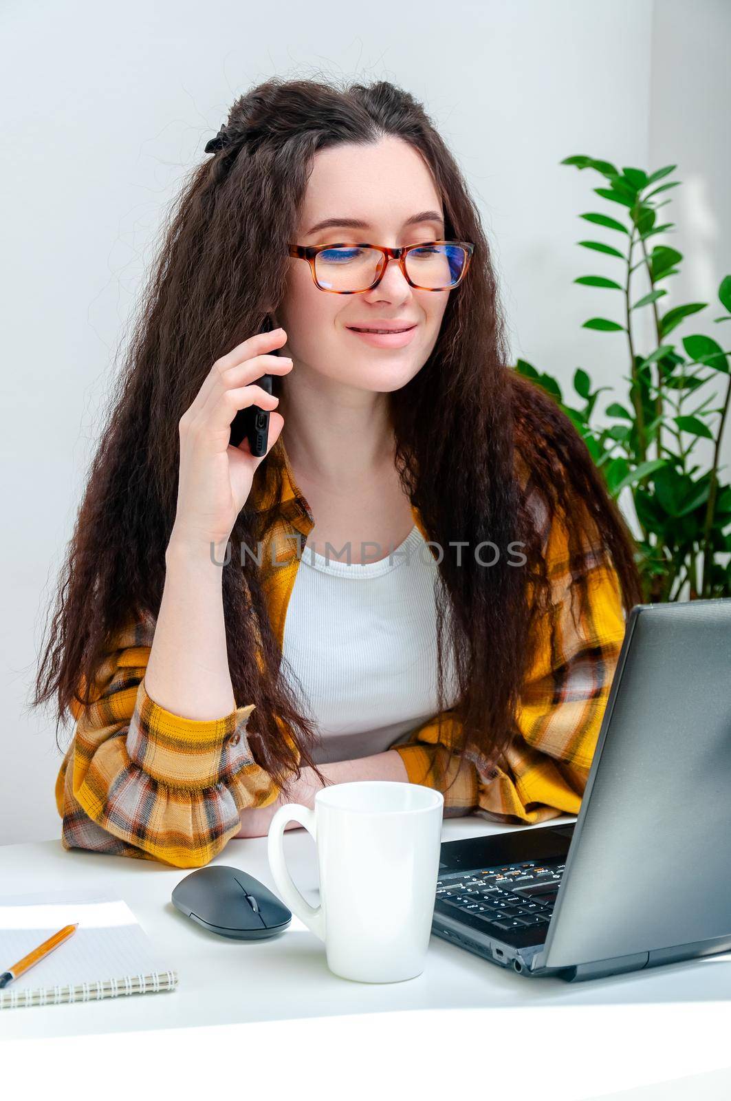 Beautiful woman in glasses talking on phone at the workplace. Woman working at home, undergoing training, watching webinar, online shopping.