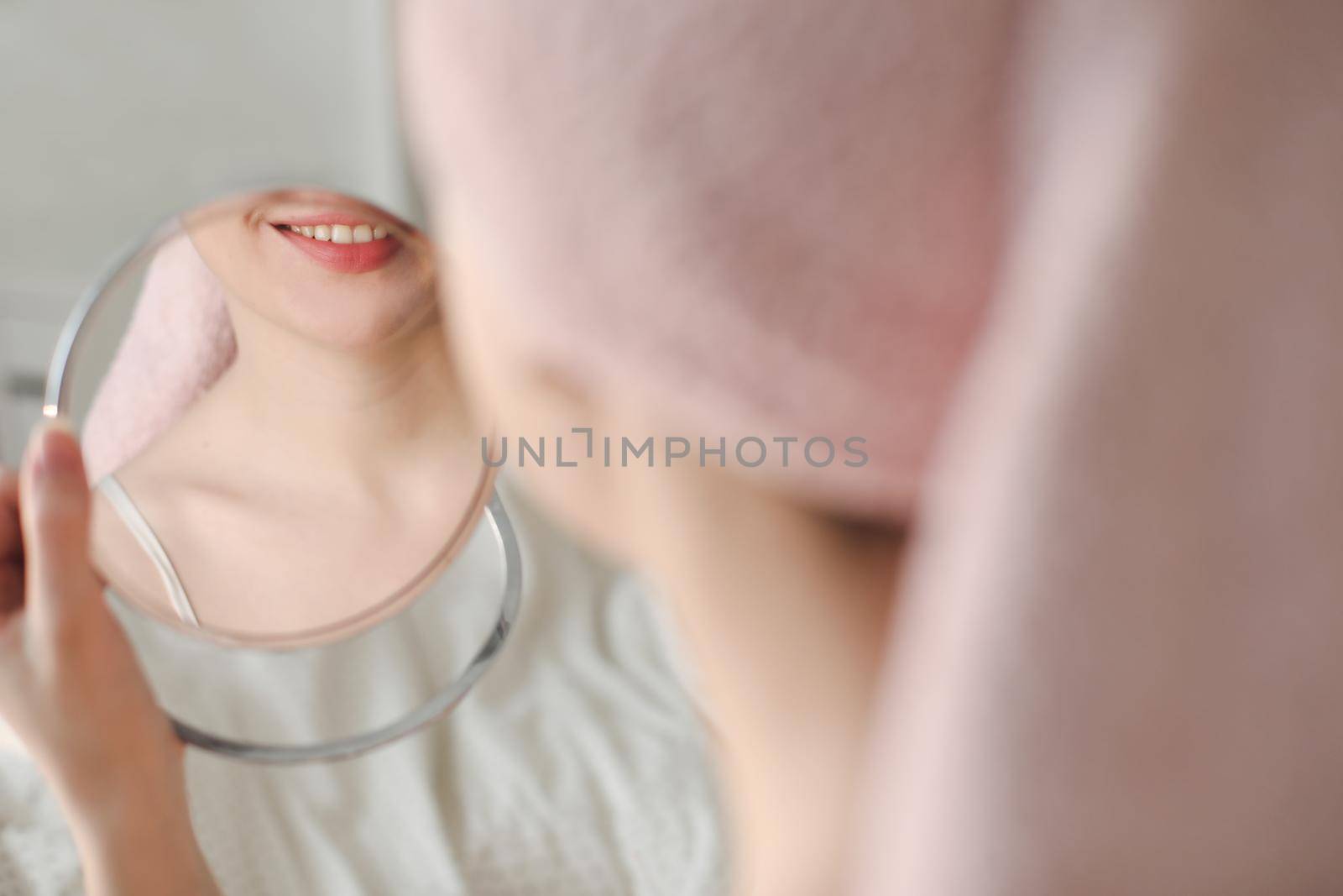 young smiling woman with a towel on head looking in the mirror. by paralisart