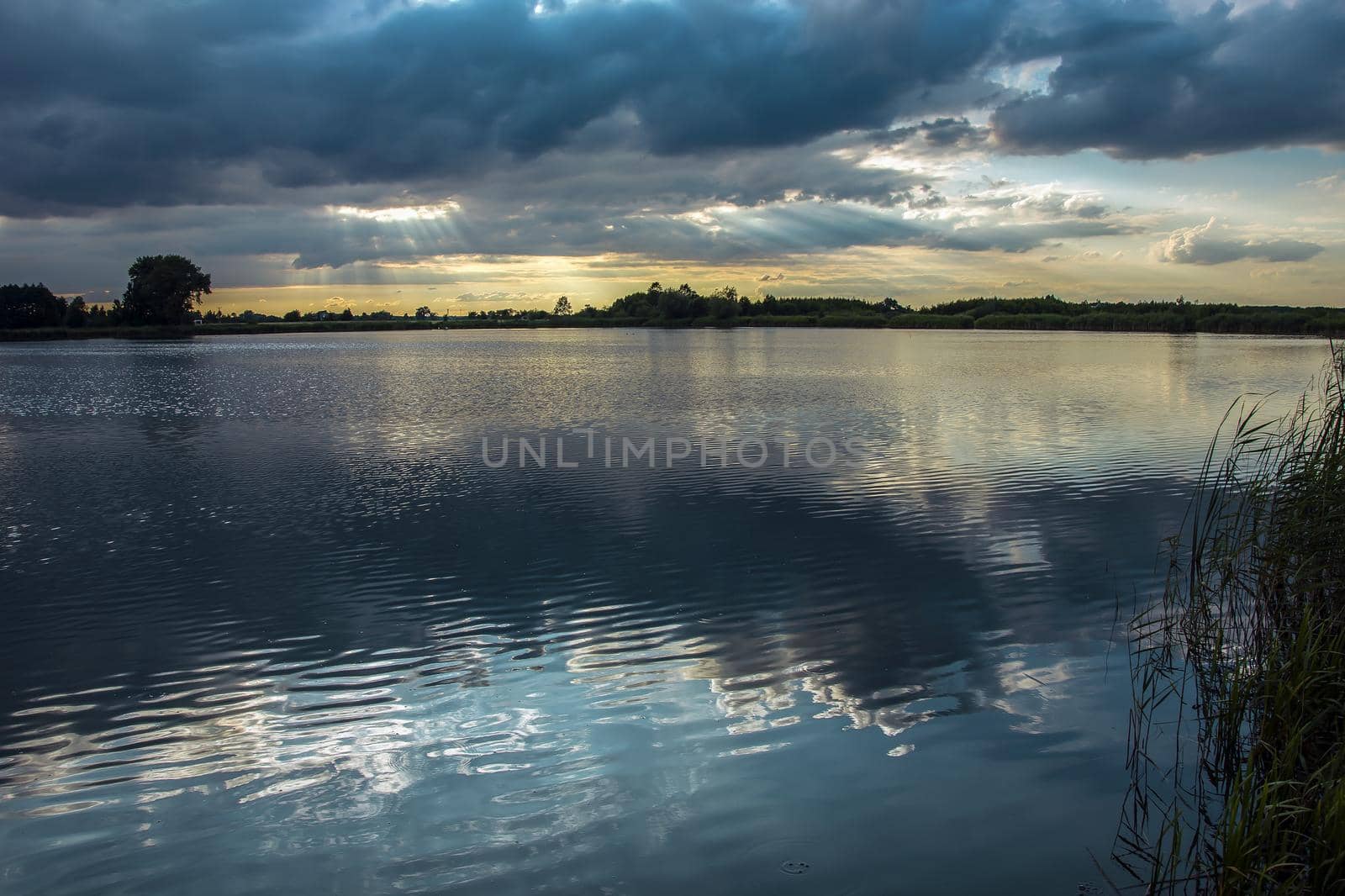 The sun's rays in the clouds over a calm lake, summer view