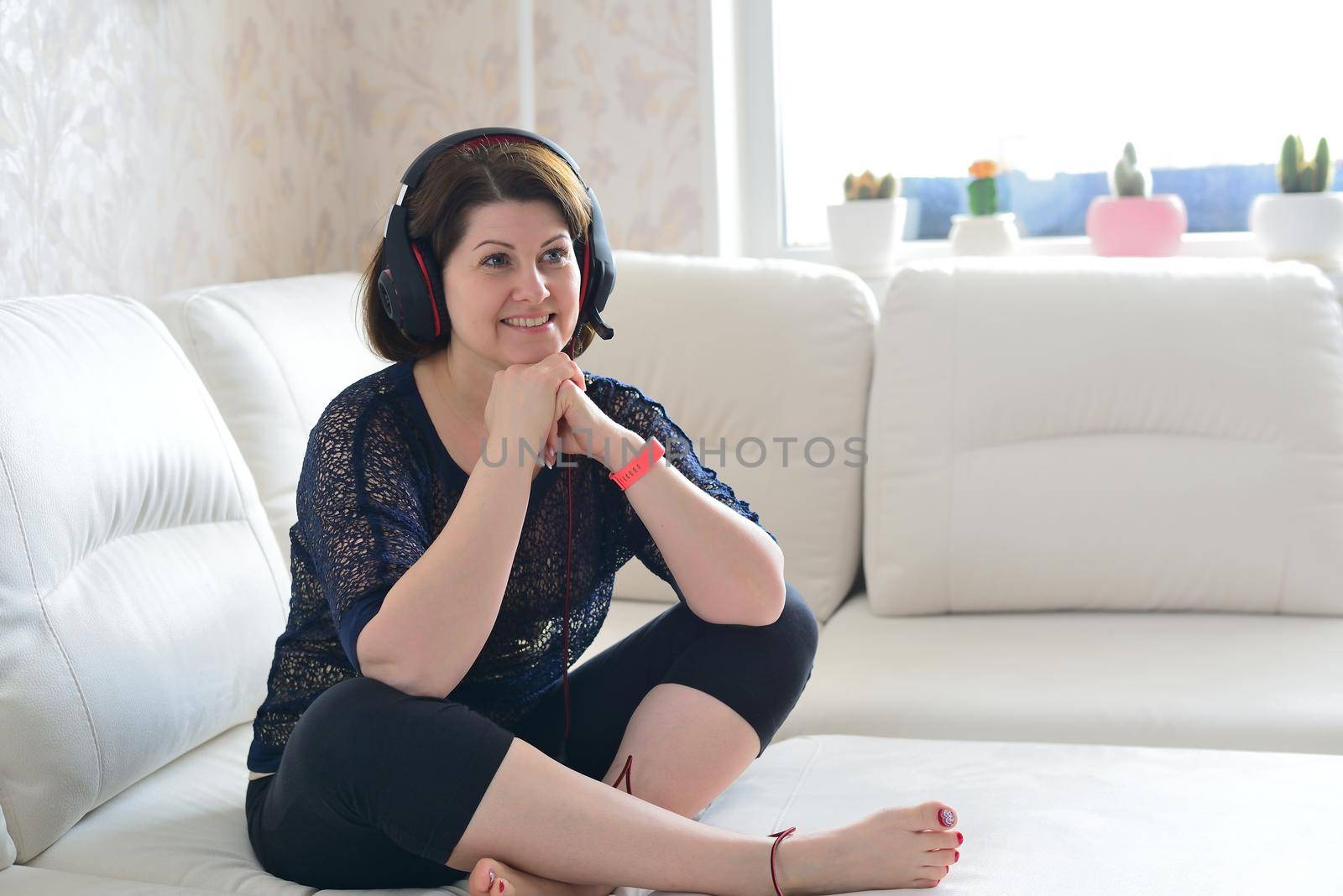 Woman in headphones listening to music while sitting on couch by olgavolodina