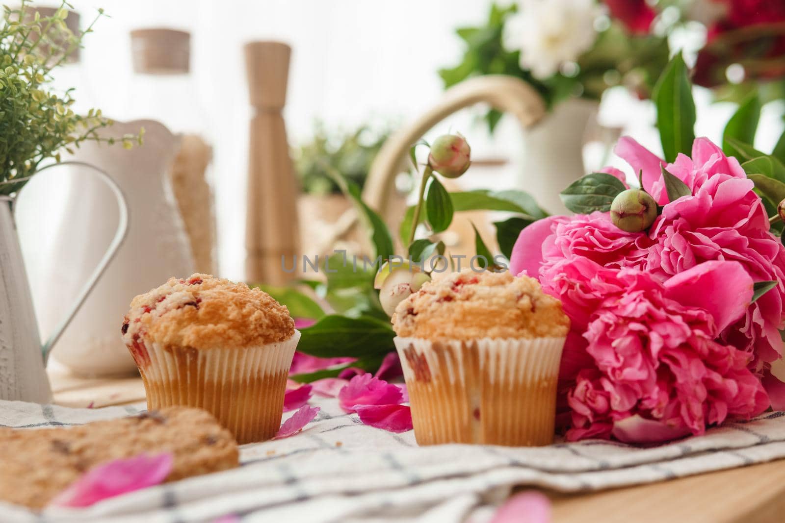 The kitchen countertop is decorated with peonies. The interior is decorated with spring flowers. Pink peonies and sweet cupcakes on a wooden countertop. Interior details