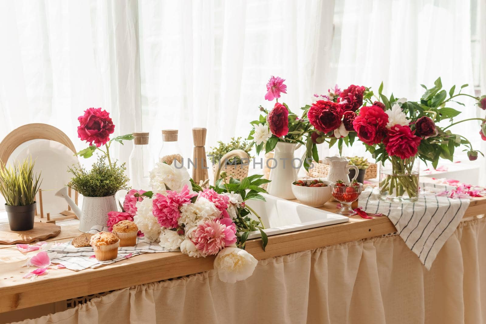 The kitchen countertop is decorated with peonies. The interior is decorated with spring flowers. Pink peonies and sweet cupcakes on a wooden countertop. Interior details
