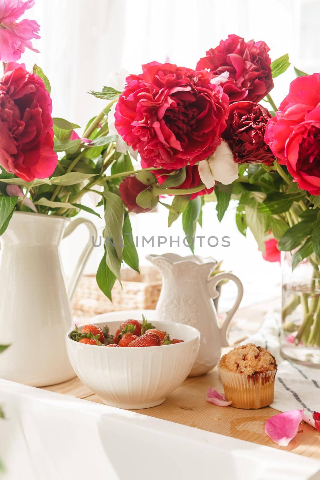 The kitchen countertop is decorated with peonies. The interior is decorated with spring flowers. Pink peonies and sweet cupcakes on a wooden countertop. Interior details