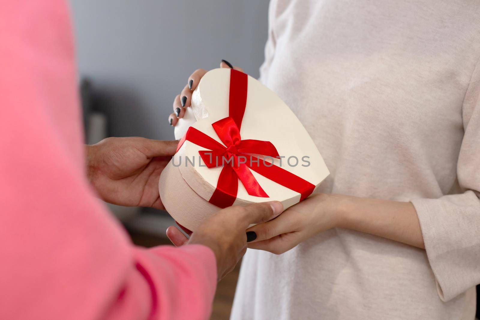 A guy in a pink jumper gives a girl in a white dress a white box in the shape of a heart. close-up