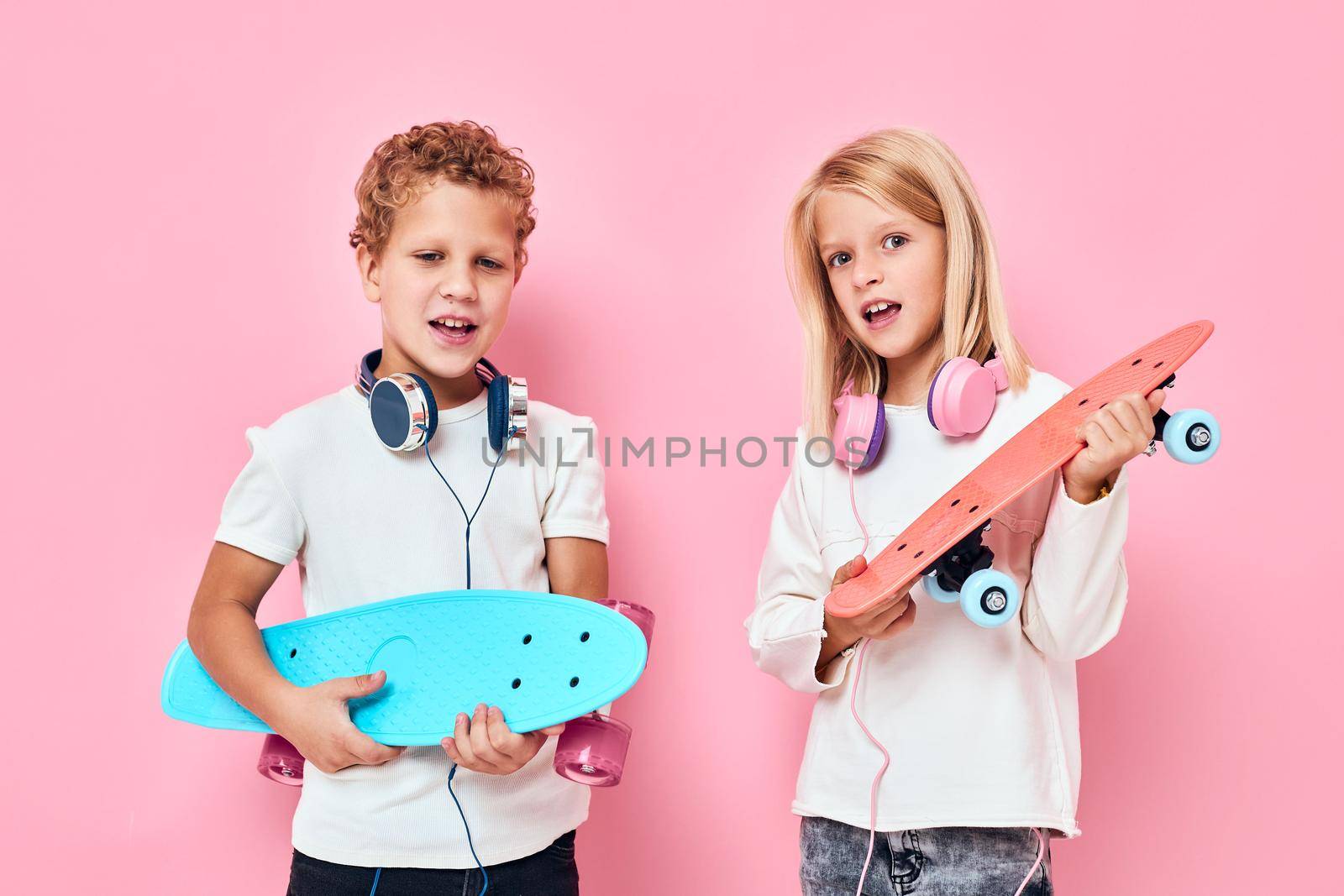 Funny children stand next to skateboards pink color background. High quality photo