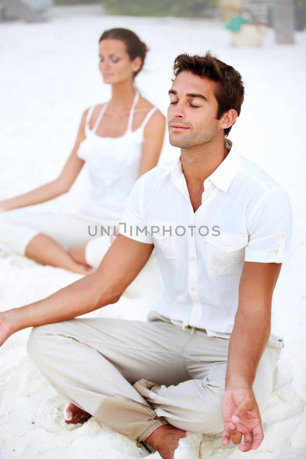 A young couple meditating in the lotus position on the beach.