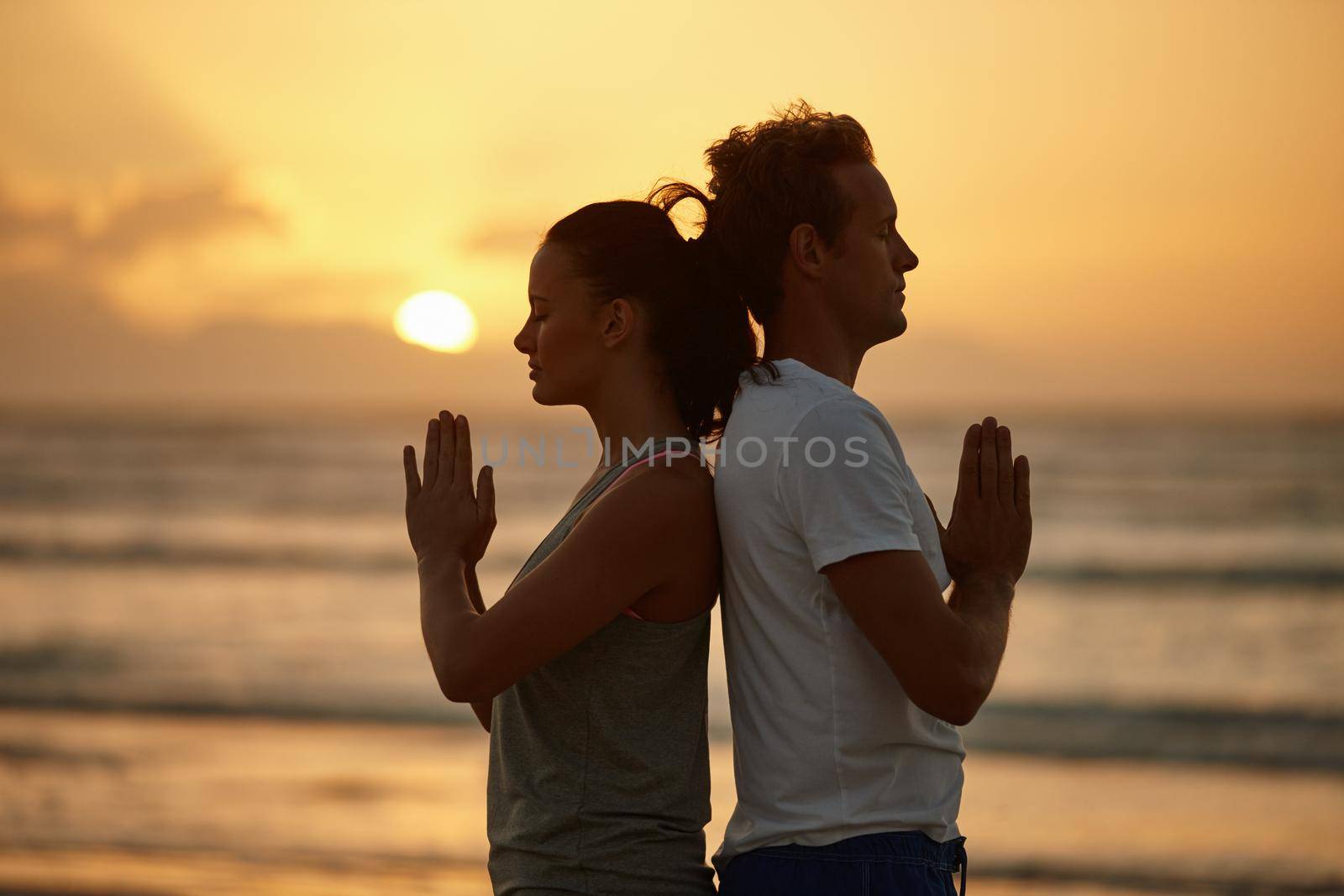 Soul experience at sunset. Shot of a couple doing yoga on the beach at sunset. by YuriArcurs